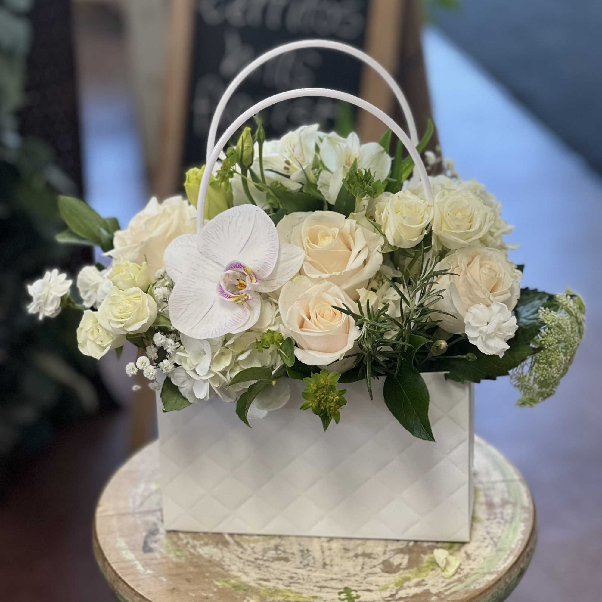 White floral arrangement in a white handled box with roses and orchids