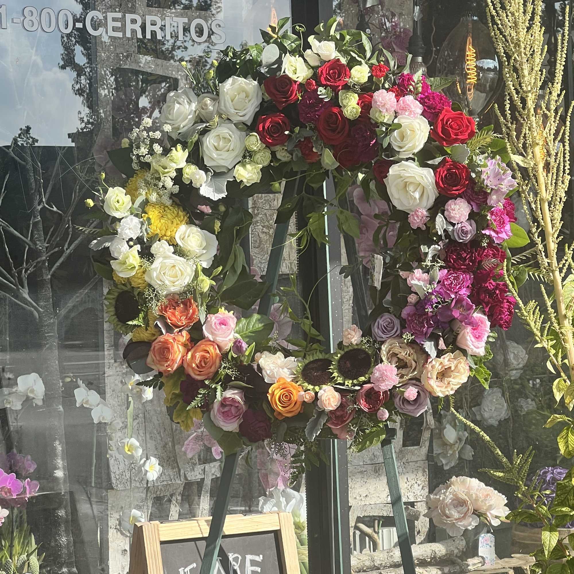 Large floral wreath on an easel with roses in red, white, pink, and orange