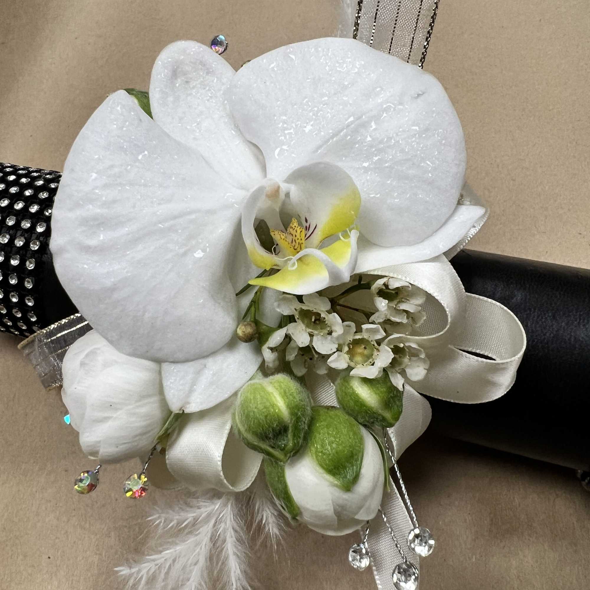 A centerpiece white phalaenopsis orchid, creamy ranunculus blooms, and glossy roses combine