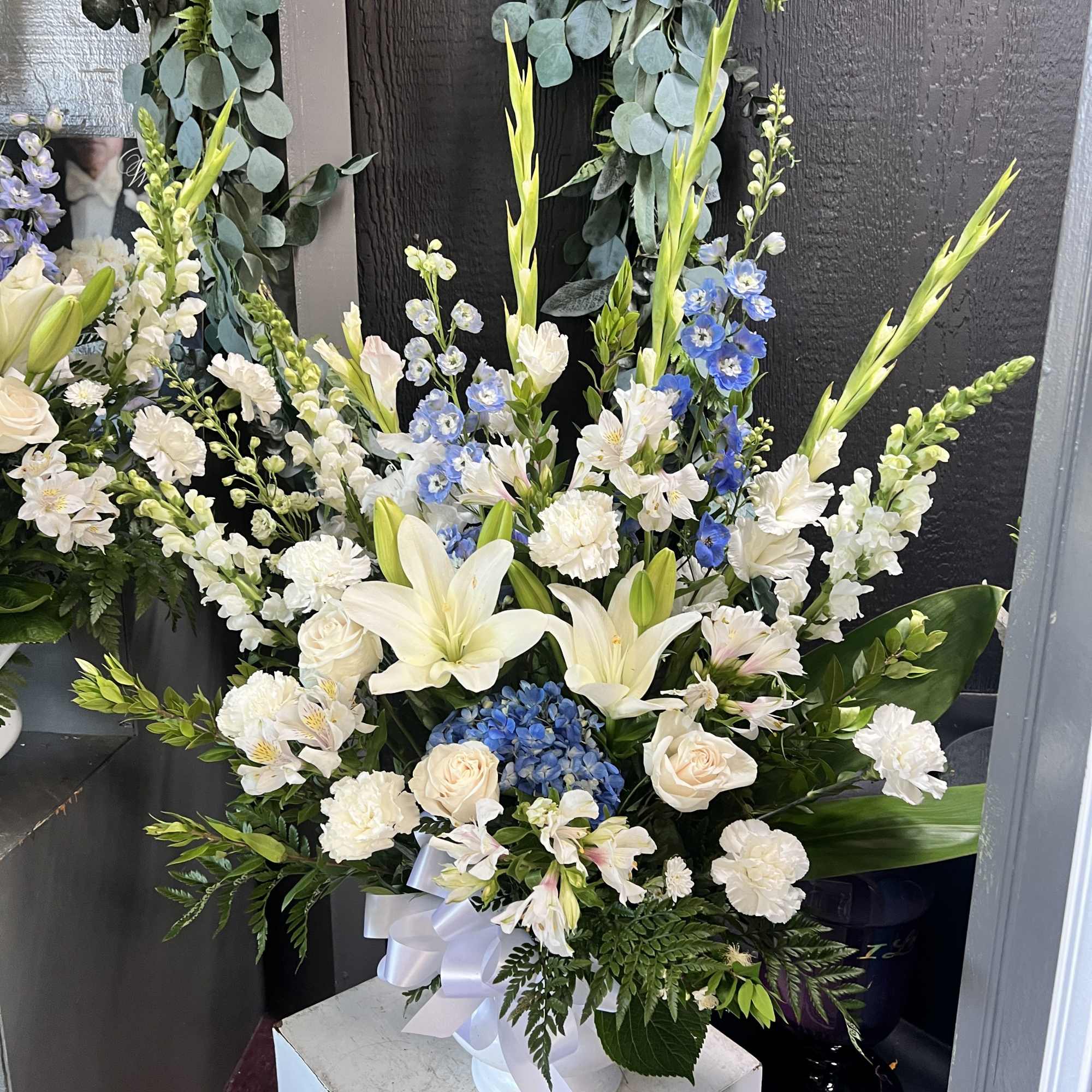 Large white floral arrangement with lilies, roses, and blue accents in a white vase
