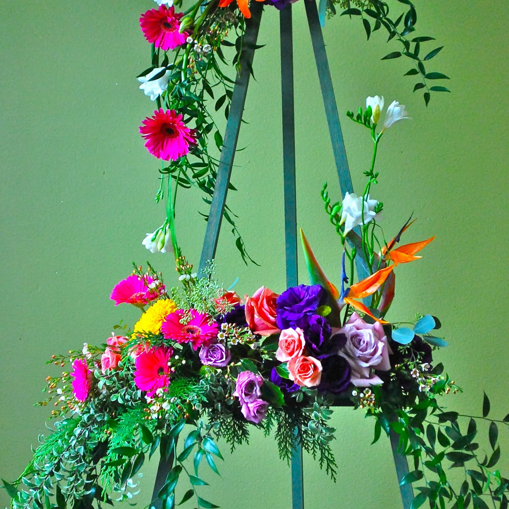 Tall floral arrangement on a metal stand with bright mixed blooms and trailing greenery