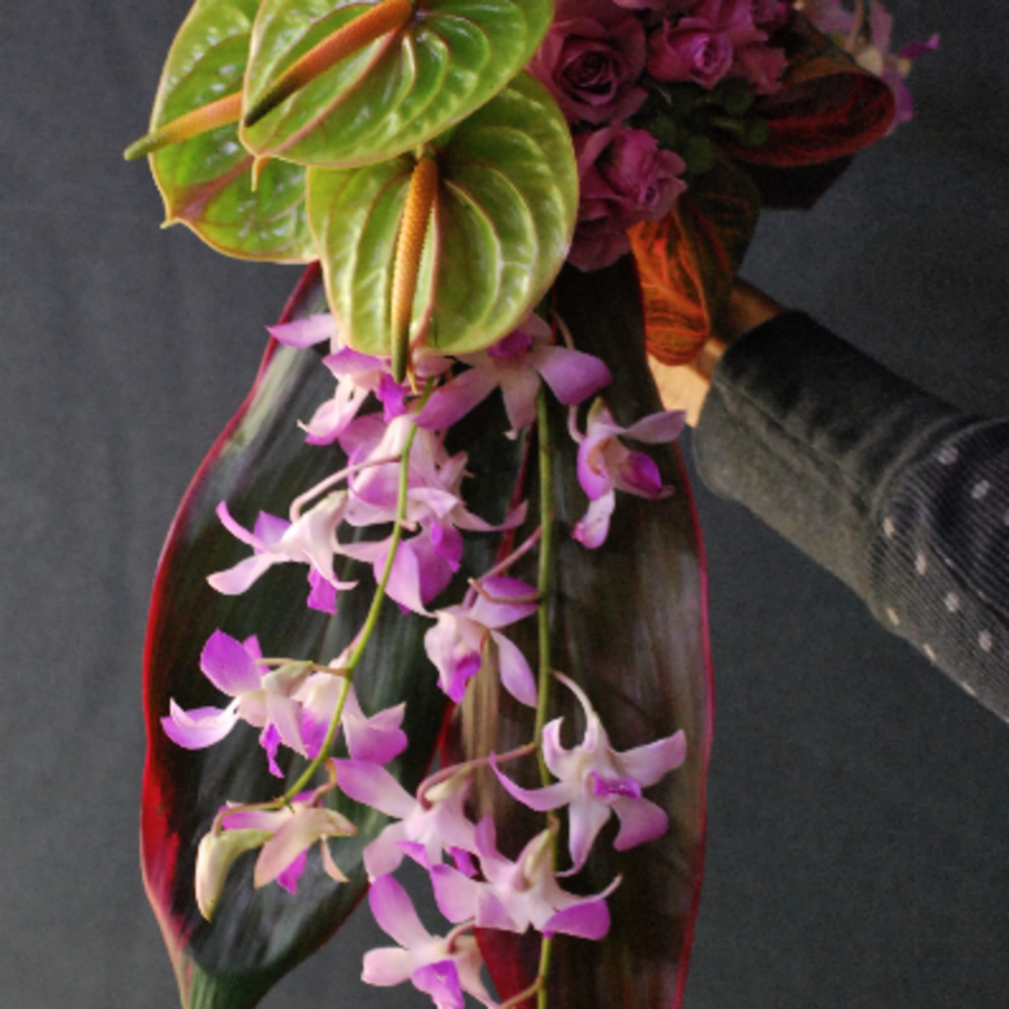 Purple rose bouquet with trailing orchid blooms and large tropical leaves