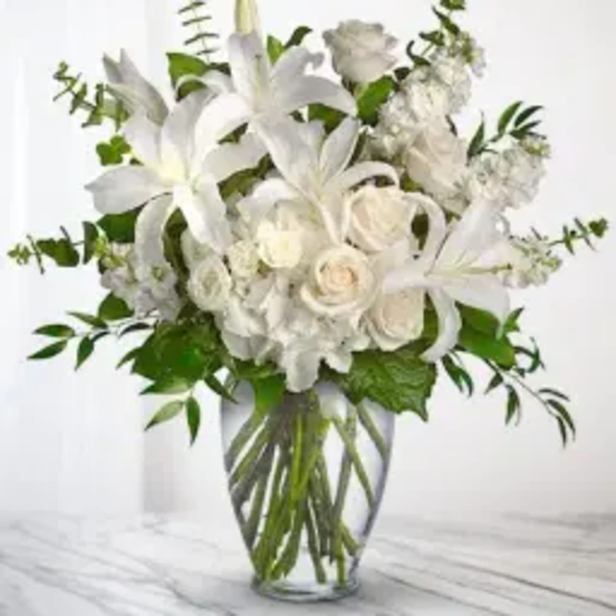 White lilies and roses in a clear glass vase with greenery