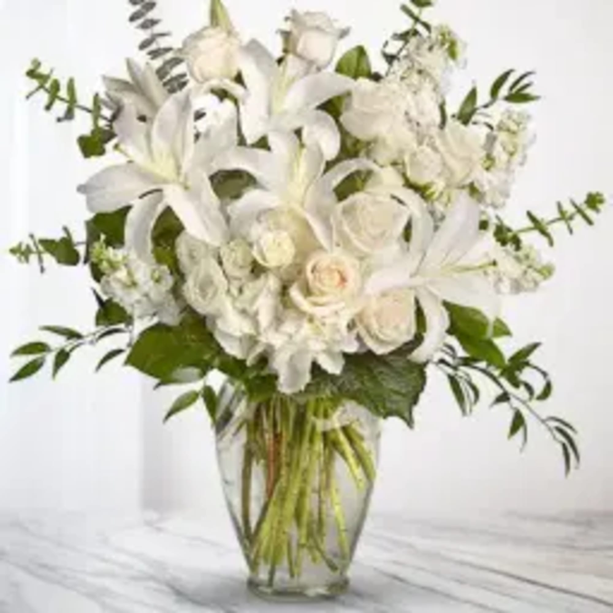 White lilies and roses arranged in a clear glass vase
