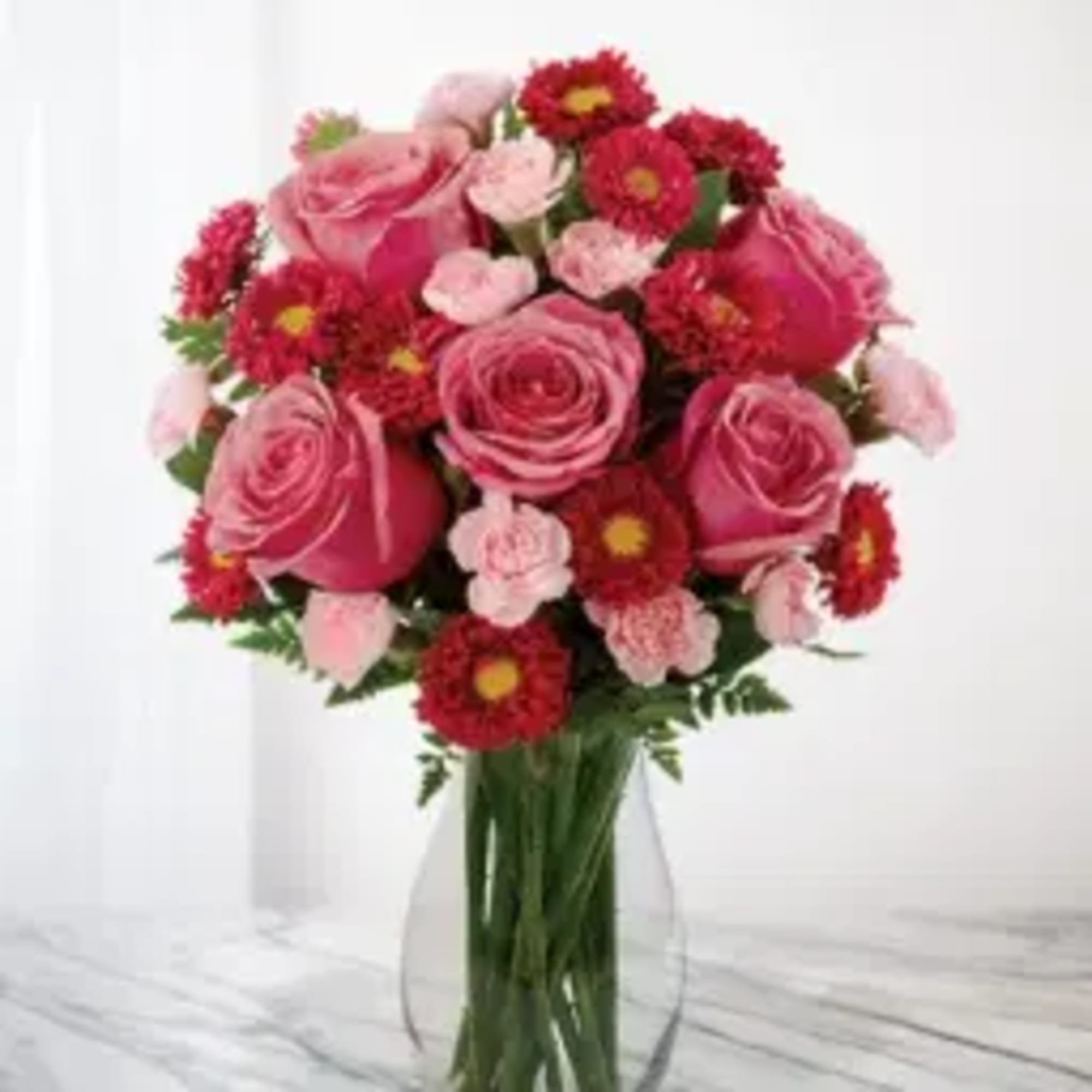 Pink roses and red daisy-like flowers arranged in a clear glass vase