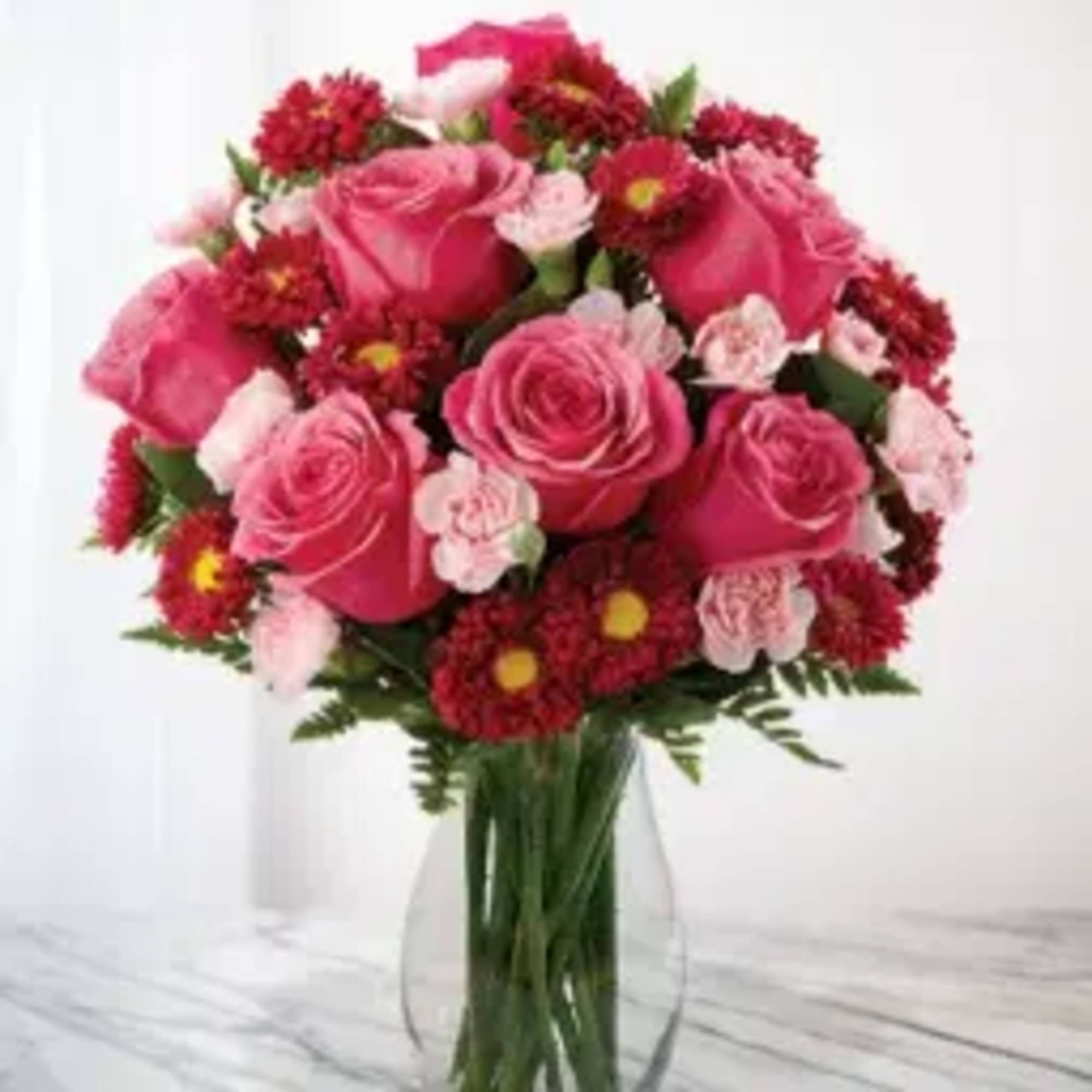 Pink roses and red daisies arranged in a clear glass vase