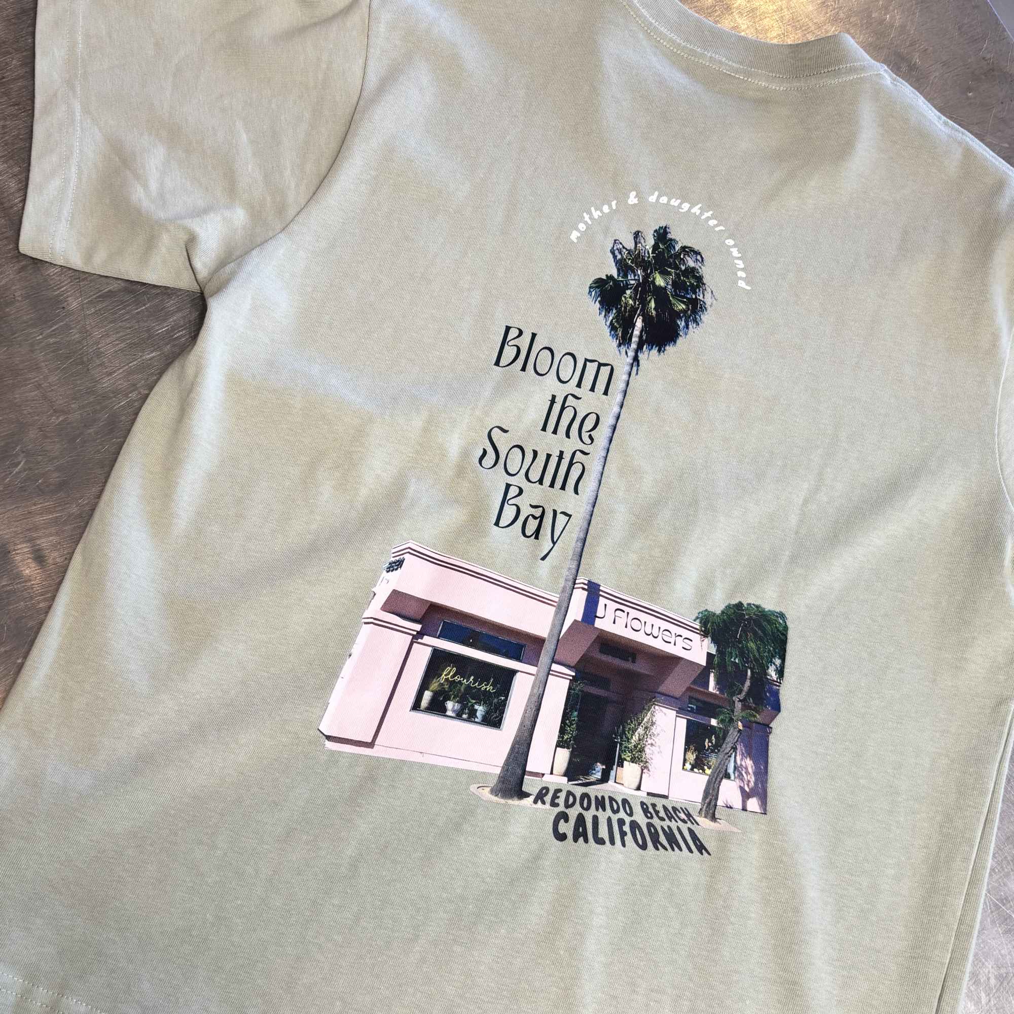 Light green T-shirt with a floral shop graphic and palm tree print