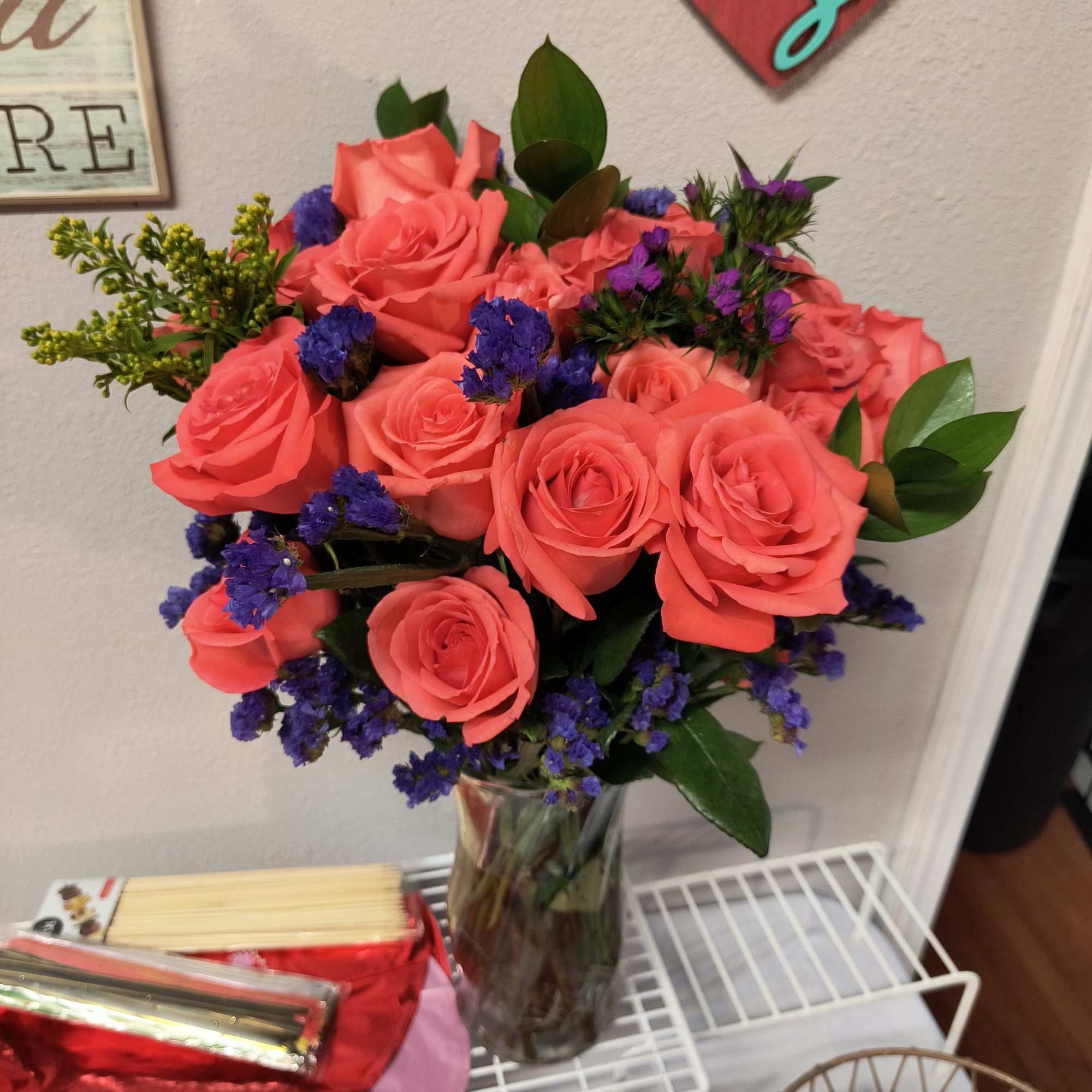 Coral rose bouquet in a clear glass vase with purple filler flowers