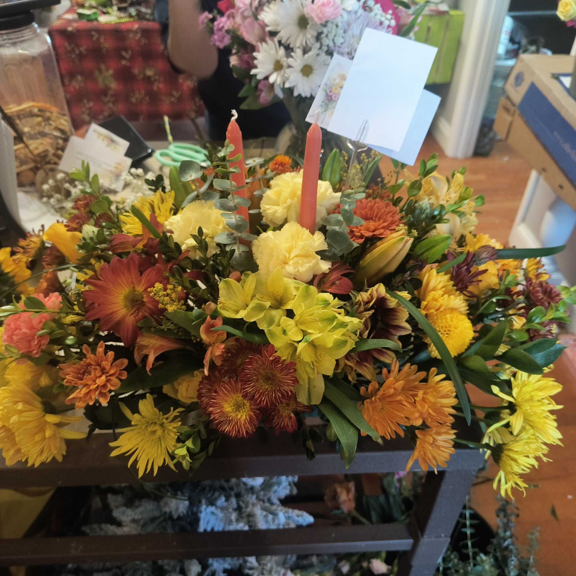 Low floral centerpiece with yellow, orange, and red blooms around two candles