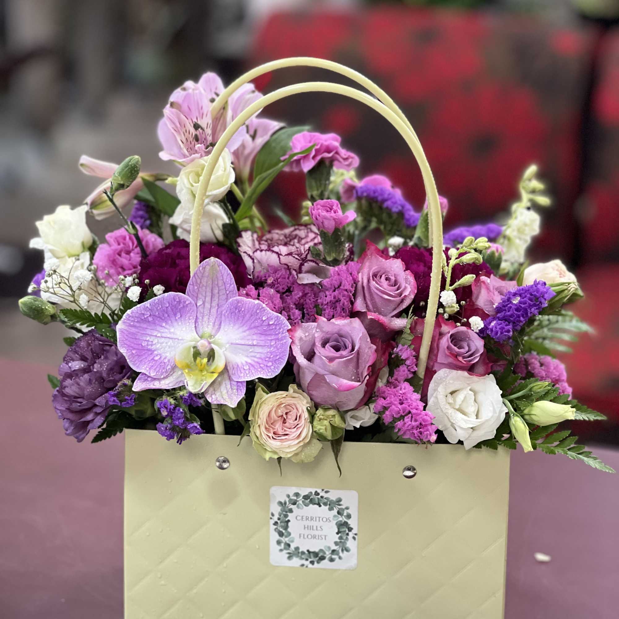 A soft lavender gift bag brimming with pink roses, white hydrangea, and