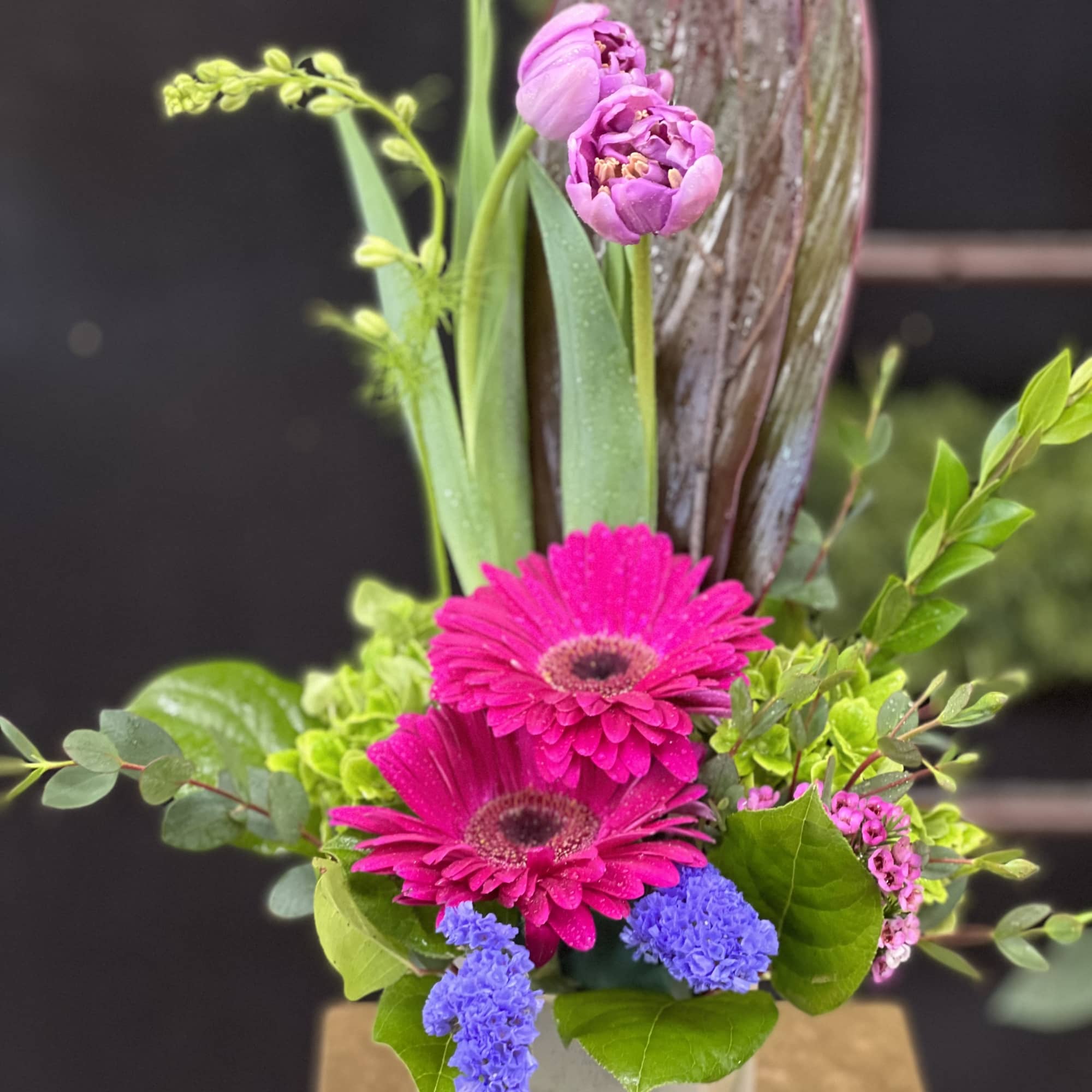 Pink gerbera daisies and purple blooms in a glass vase