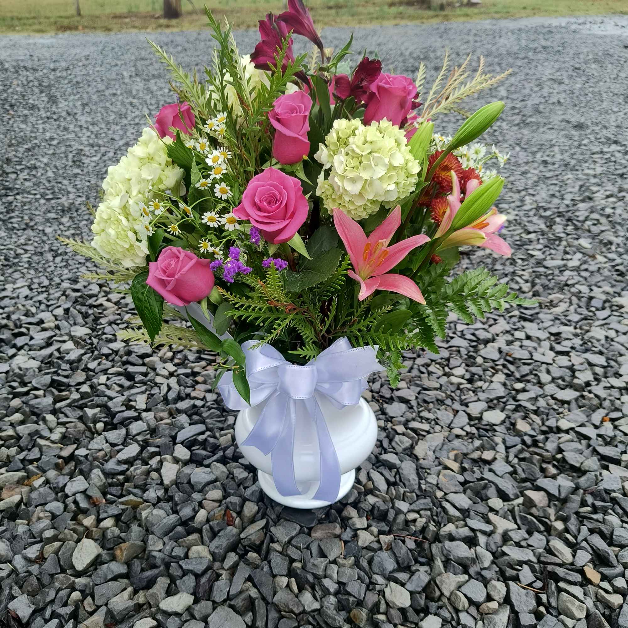 Pink roses and lilies arranged in a white vase with a ribbon