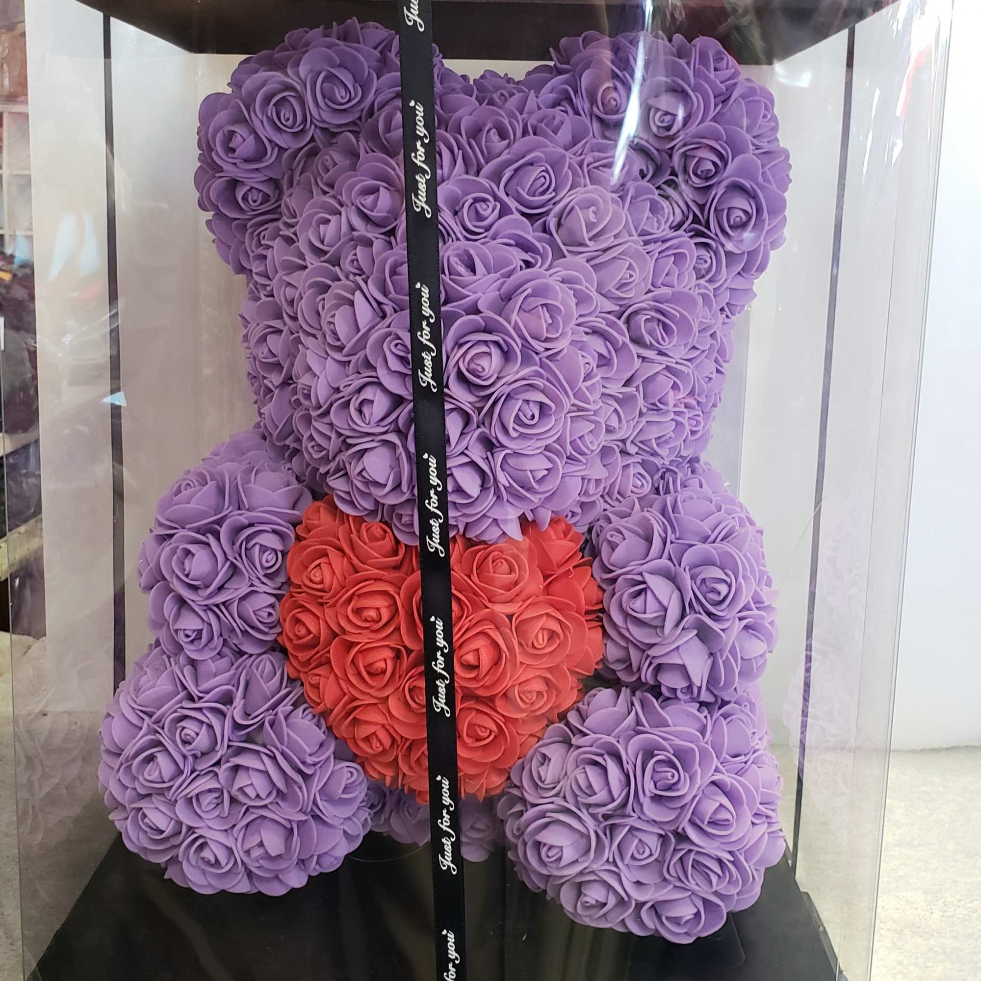 Purple teddy bear made of roses in a clear gift box with a red heart