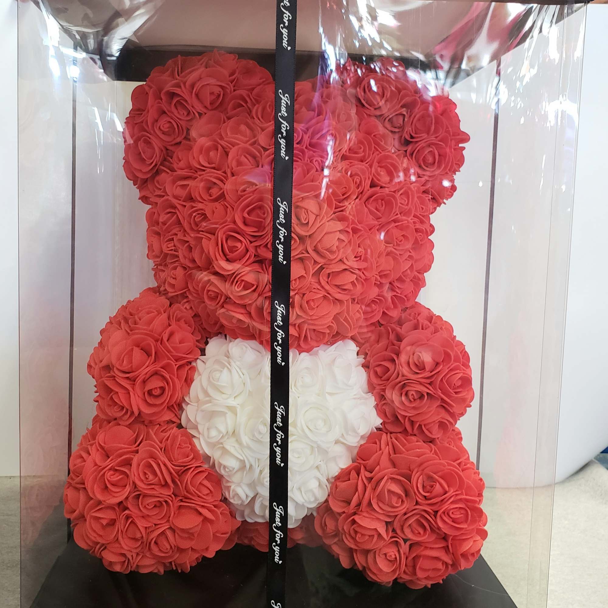 Red teddy bear made of roses in a clear gift box with a white heart
