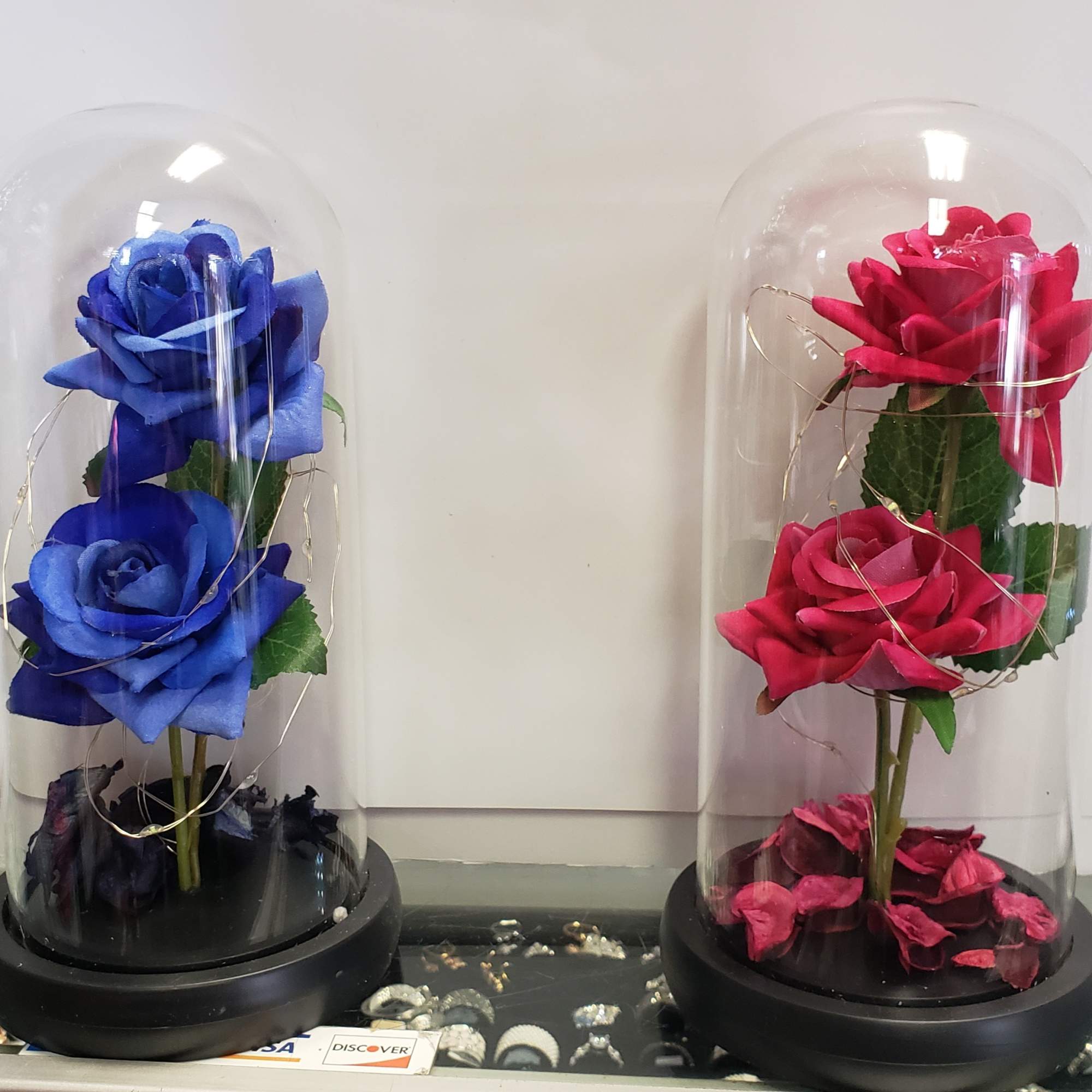 Two artificial roses under clear glass domes on black bases