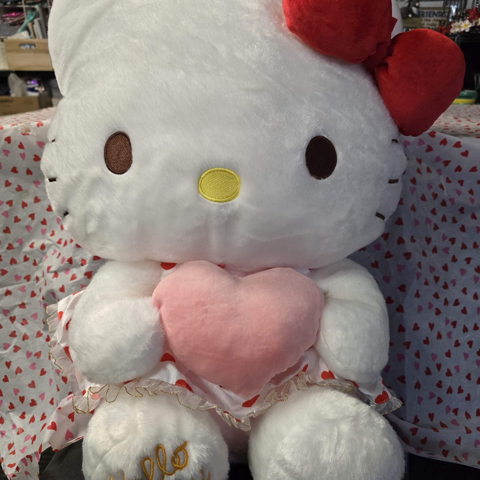 Hello Kitty plush holding a pink heart, with red bows and heart-patterned fabric