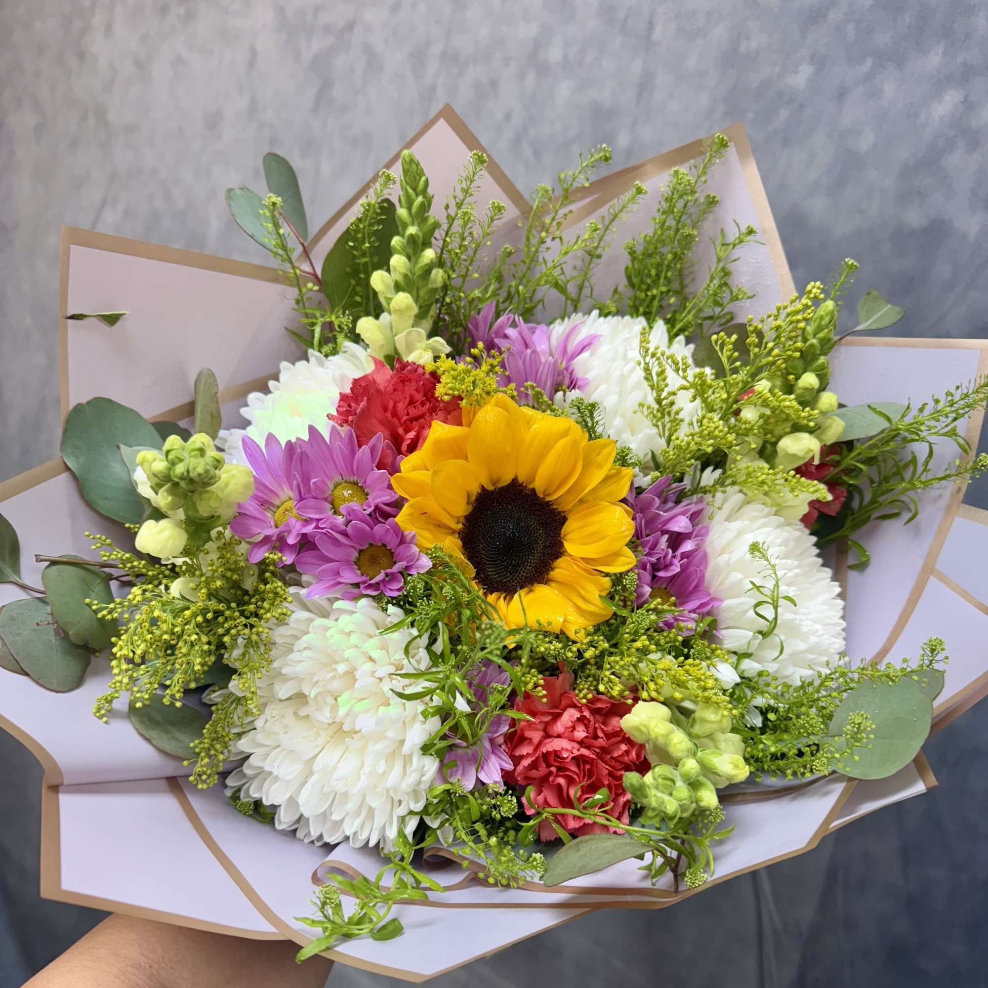 Bouquet with a sunflower, chrysanthemums, and carnations in pastel wrap