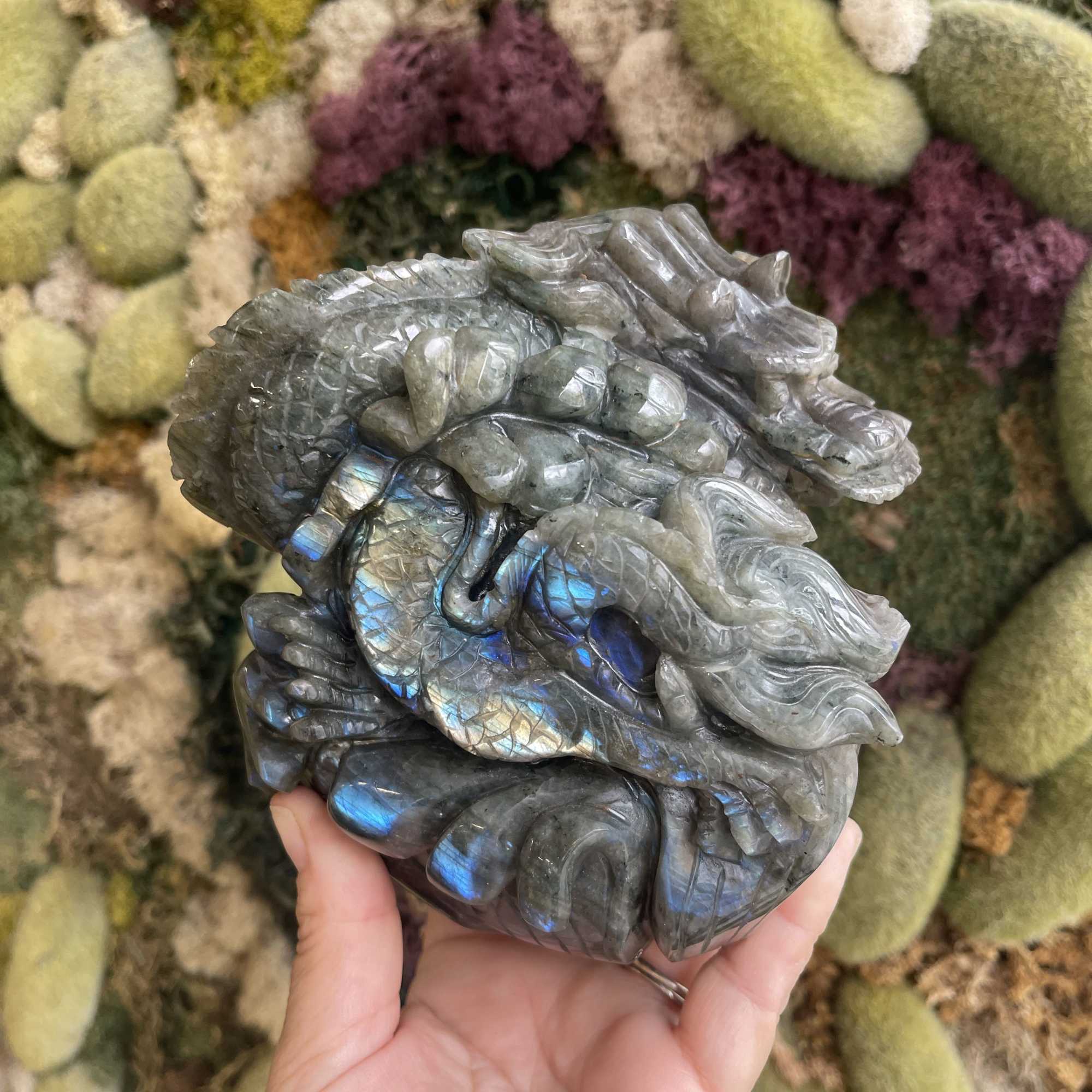 Hand holding a polished iridescent stone in front of a floral wall
