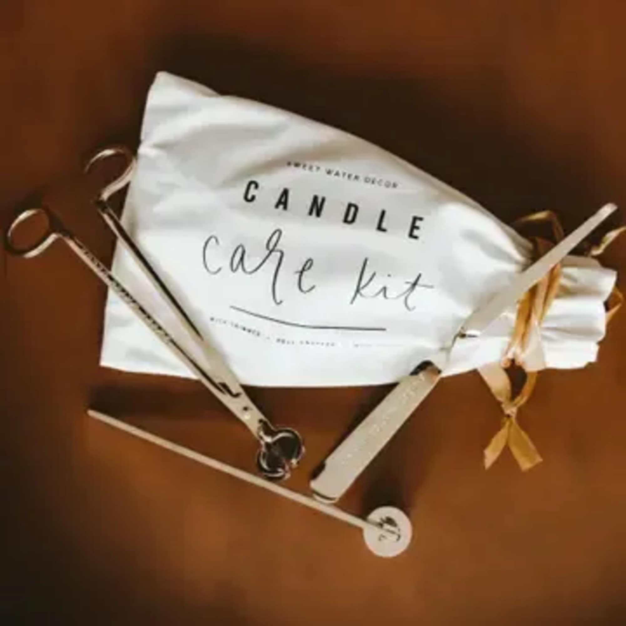 Candle care kit tools and white drawstring pouch on a brown surface