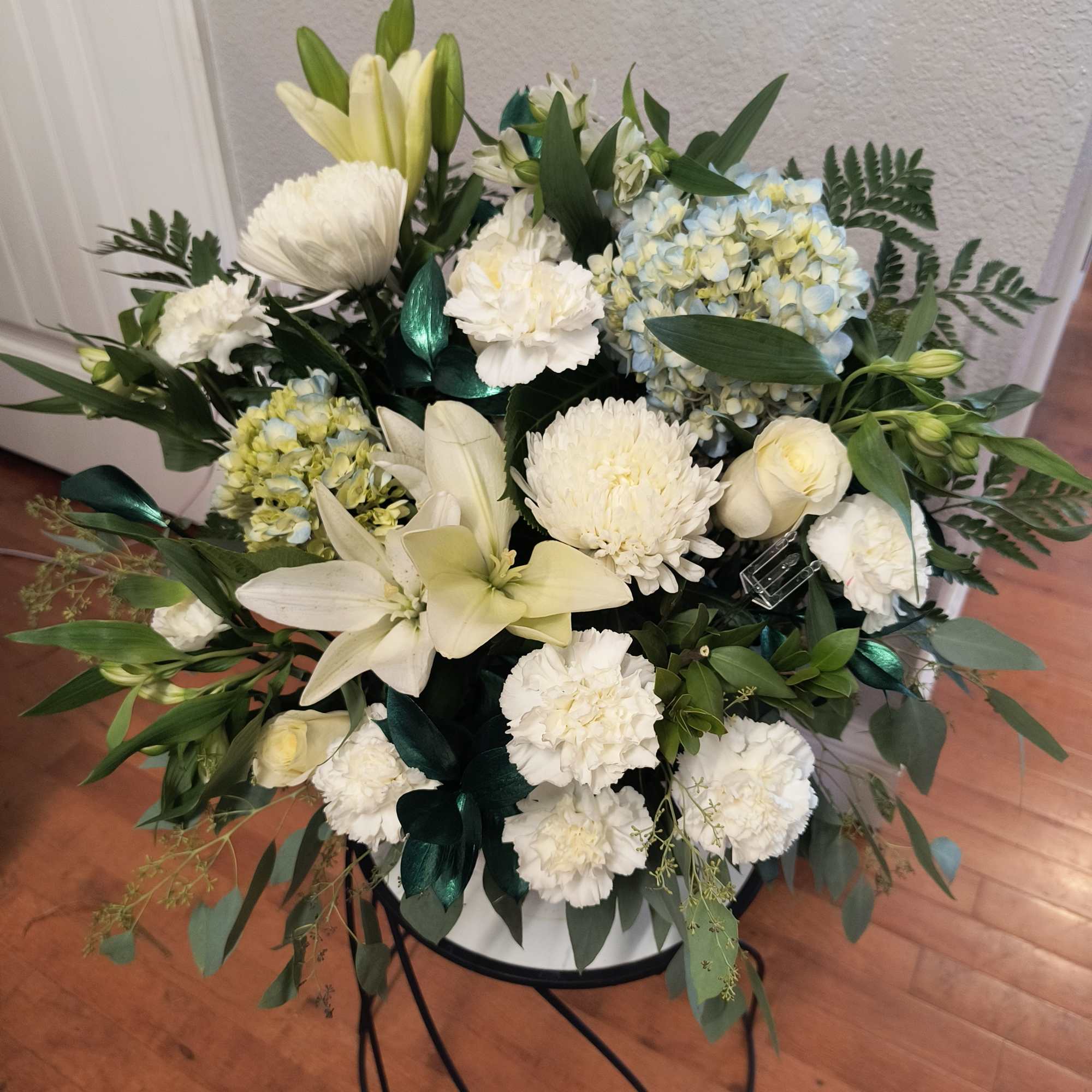 White floral arrangement with lilies, hydrangeas, and chrysanthemums in a round stand
