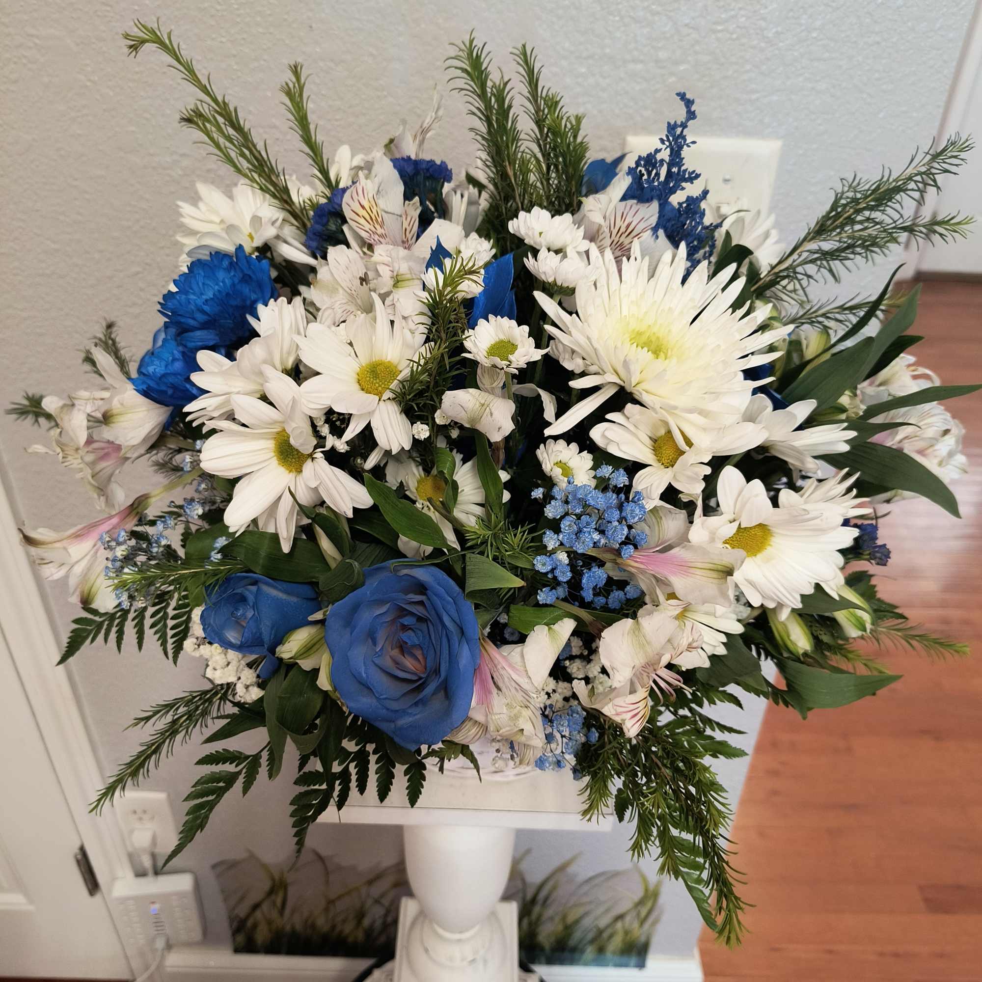 Blue and white mixed flower arrangement in a white pedestal vase