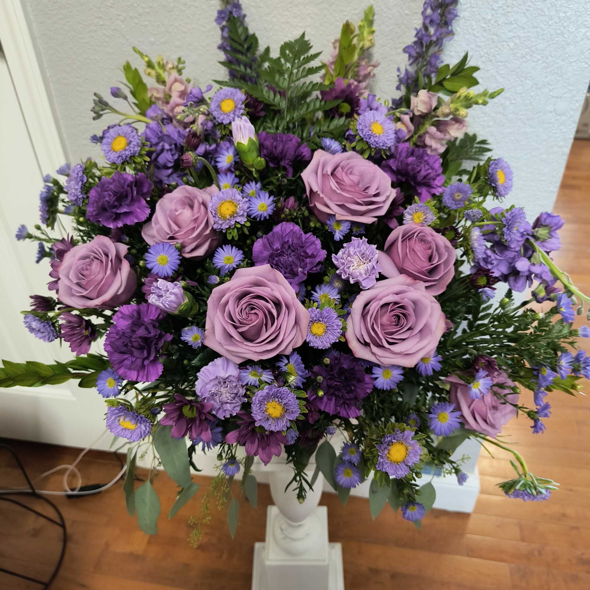 Lavender roses and purple mixed flowers arranged in a white pedestal vase