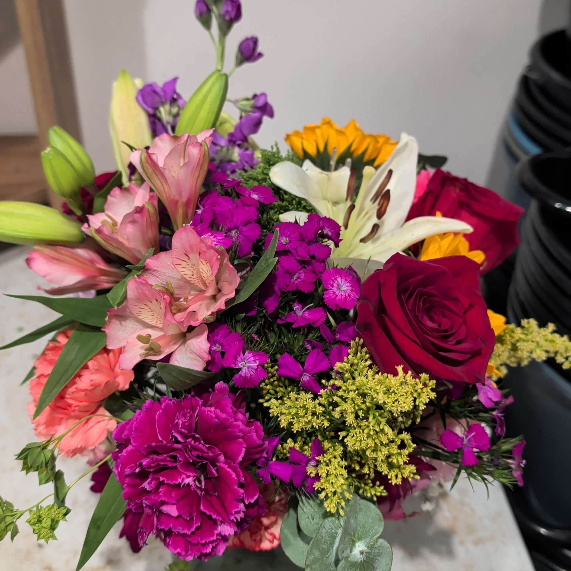 Mixed bouquet with roses, lilies, carnations, and purple filler flowers in a vase