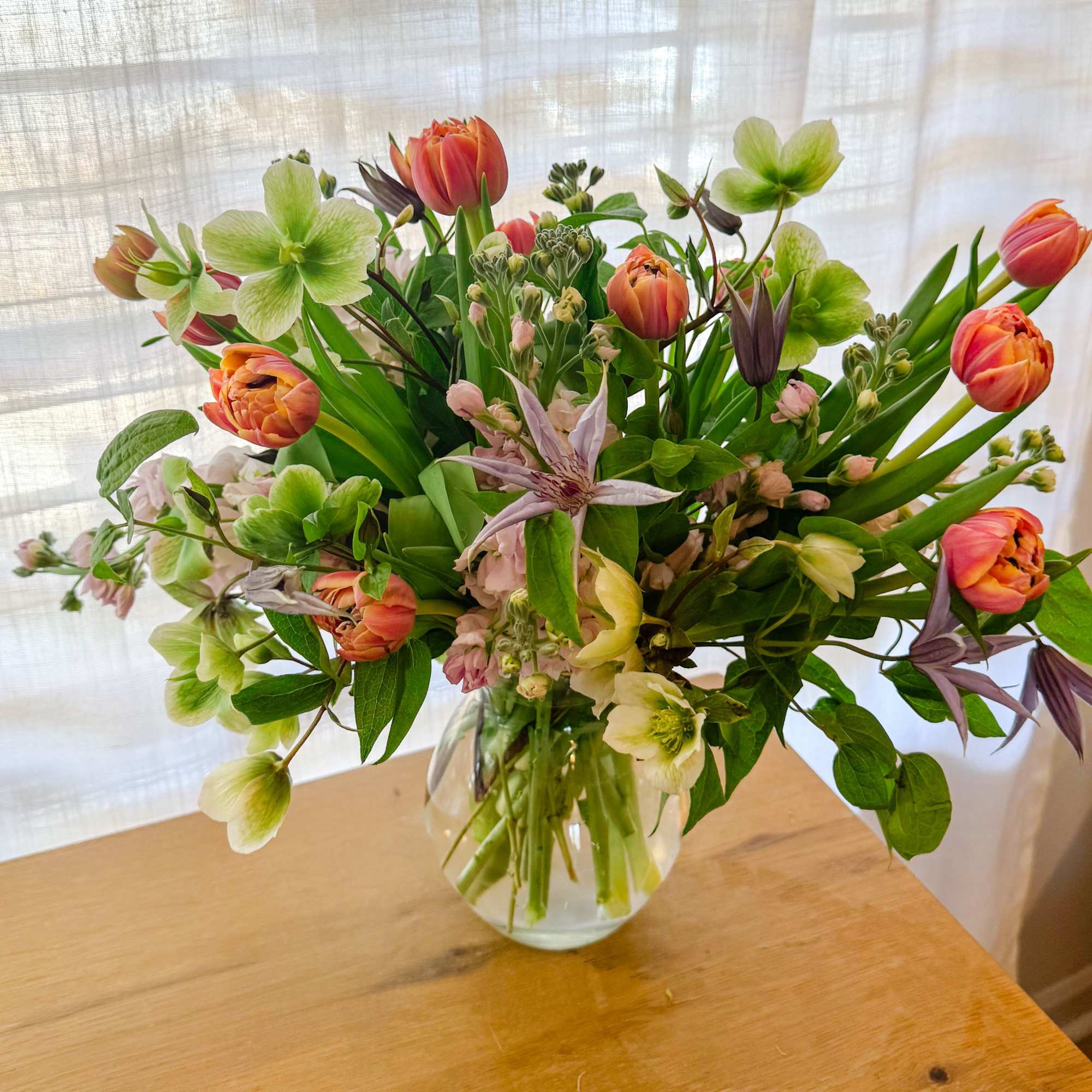 Mixed bouquet of orange tulips and pale green flowers in a glass vase