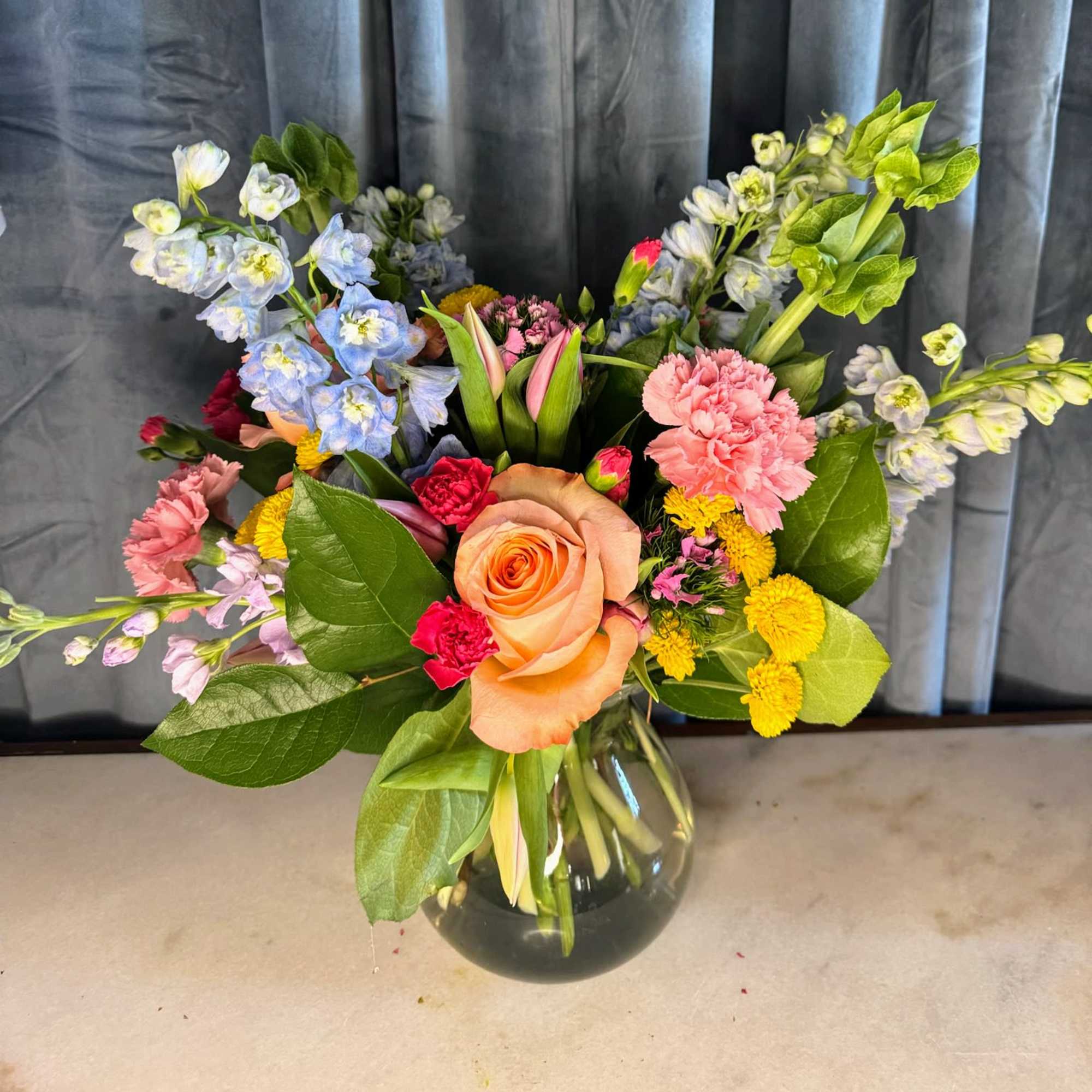 Mixed bouquet with peach roses, pink carnations, and blue flowers in a glass vase