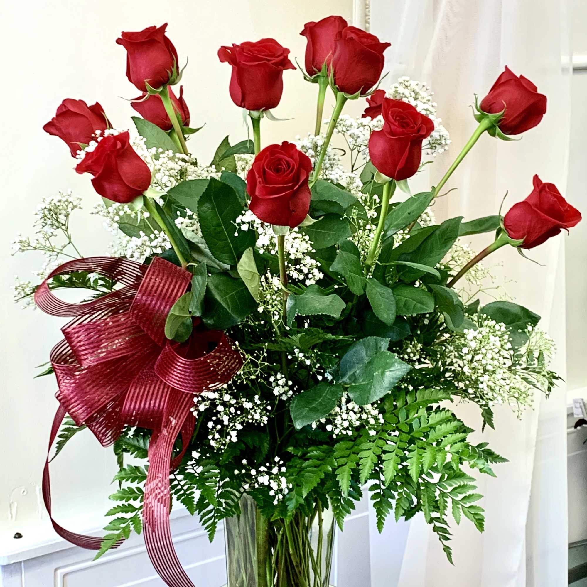 Red roses in a clear glass vase with white baby's breath and a burgundy ribbon