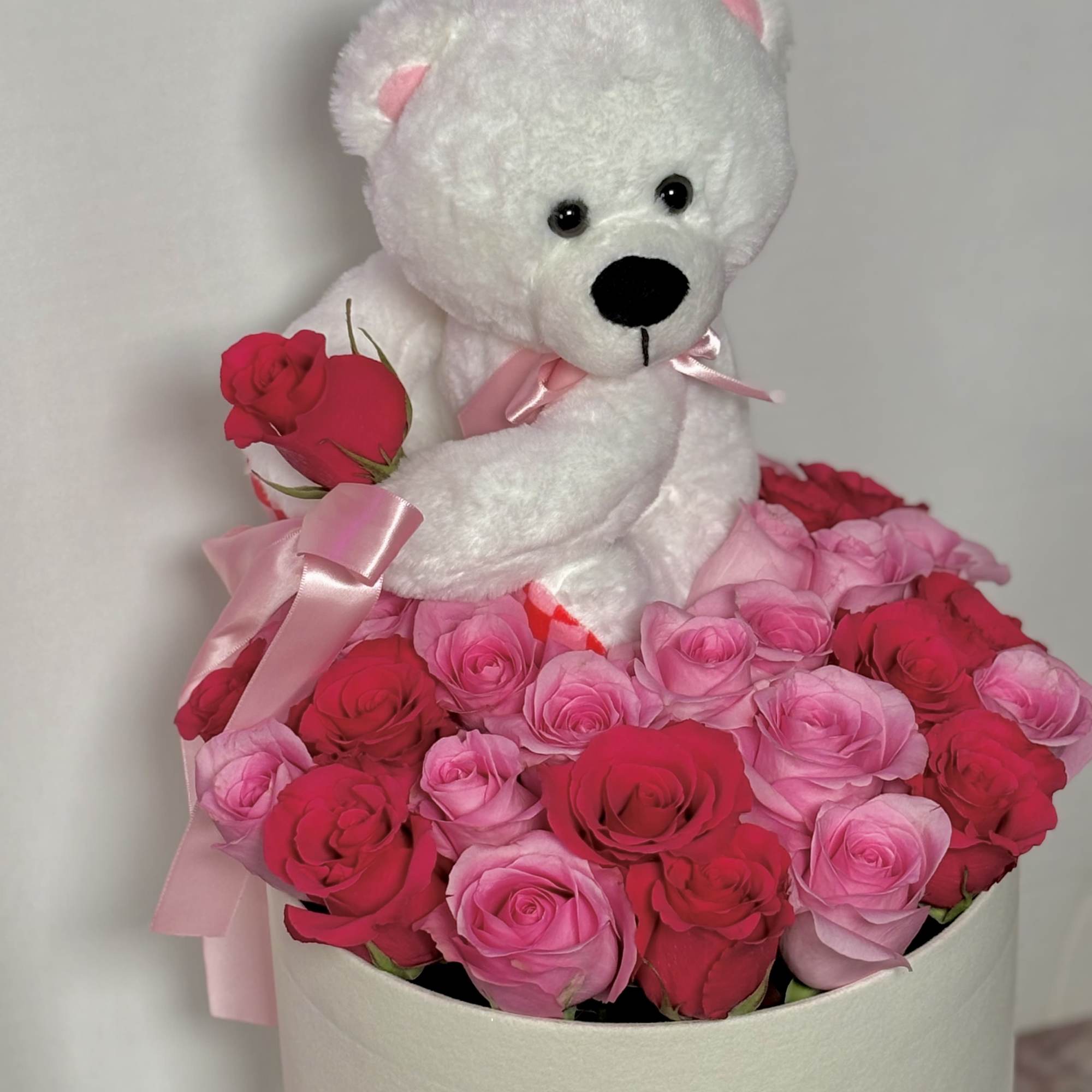 White teddy bear holding pink roses in a box of pink and red roses