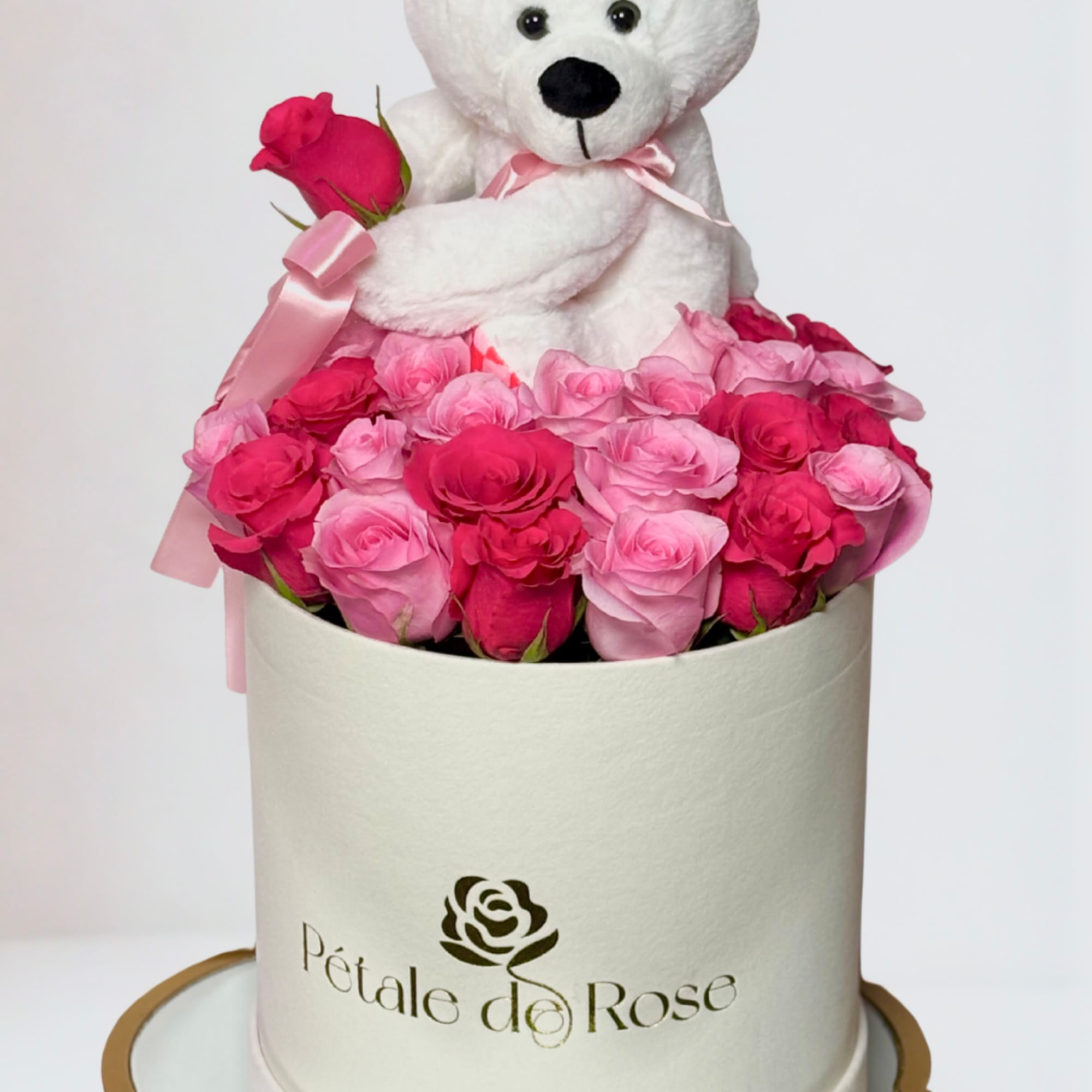 White teddy bear sitting in a box of pink roses with a ribbon