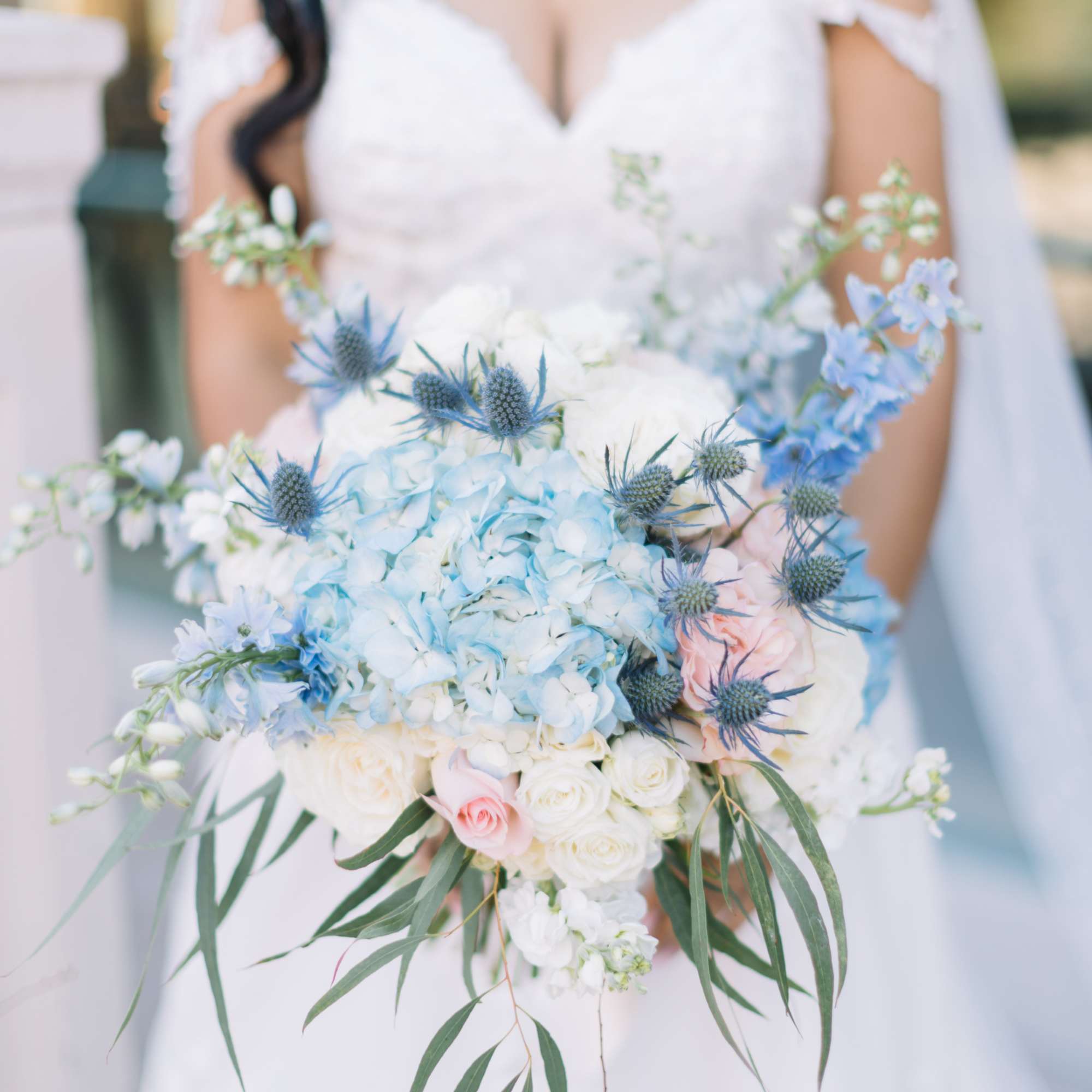 Bride holding a pastel blue and white bouquet with roses and thistle