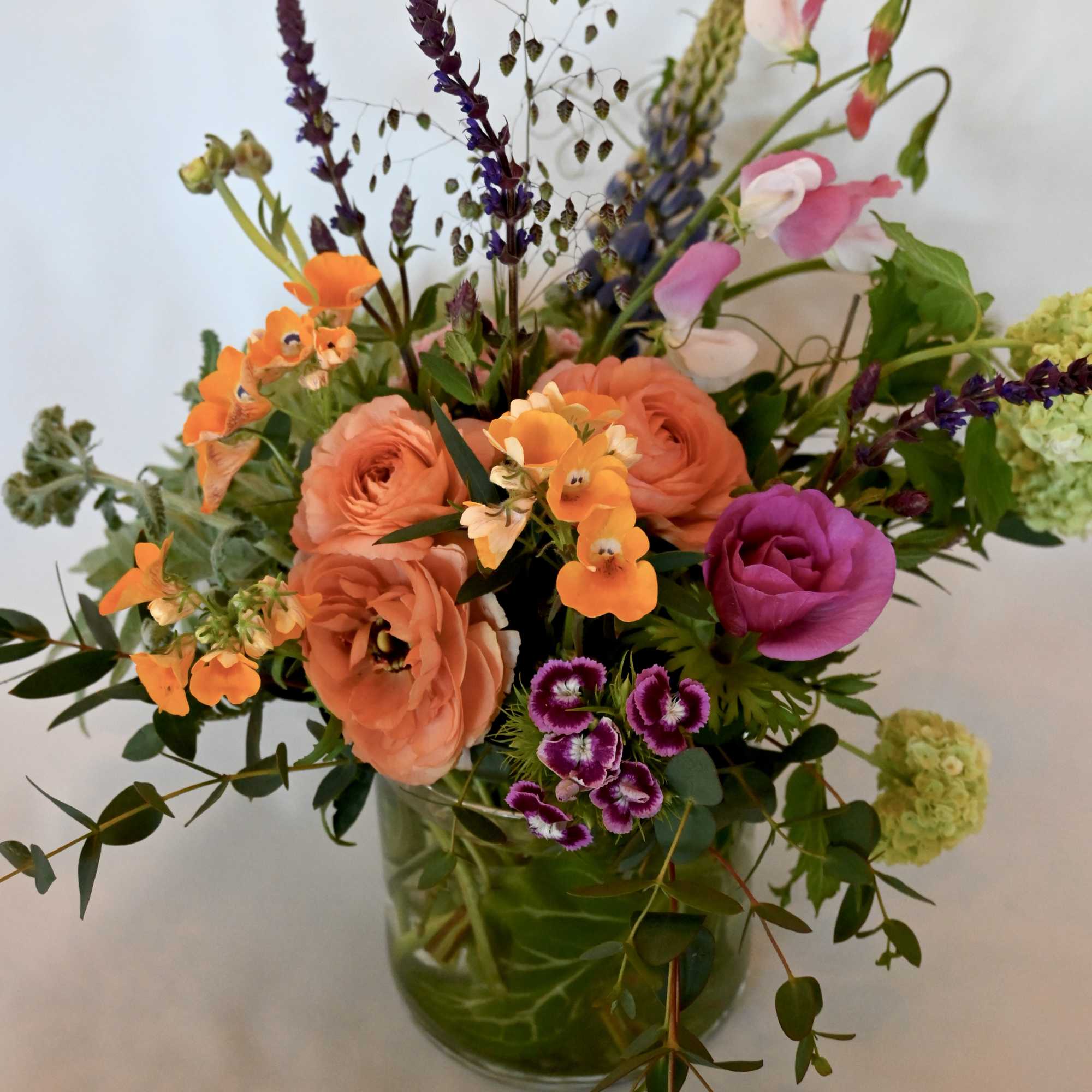 Mixed bouquet of peach, pink, and purple flowers in a glass vase