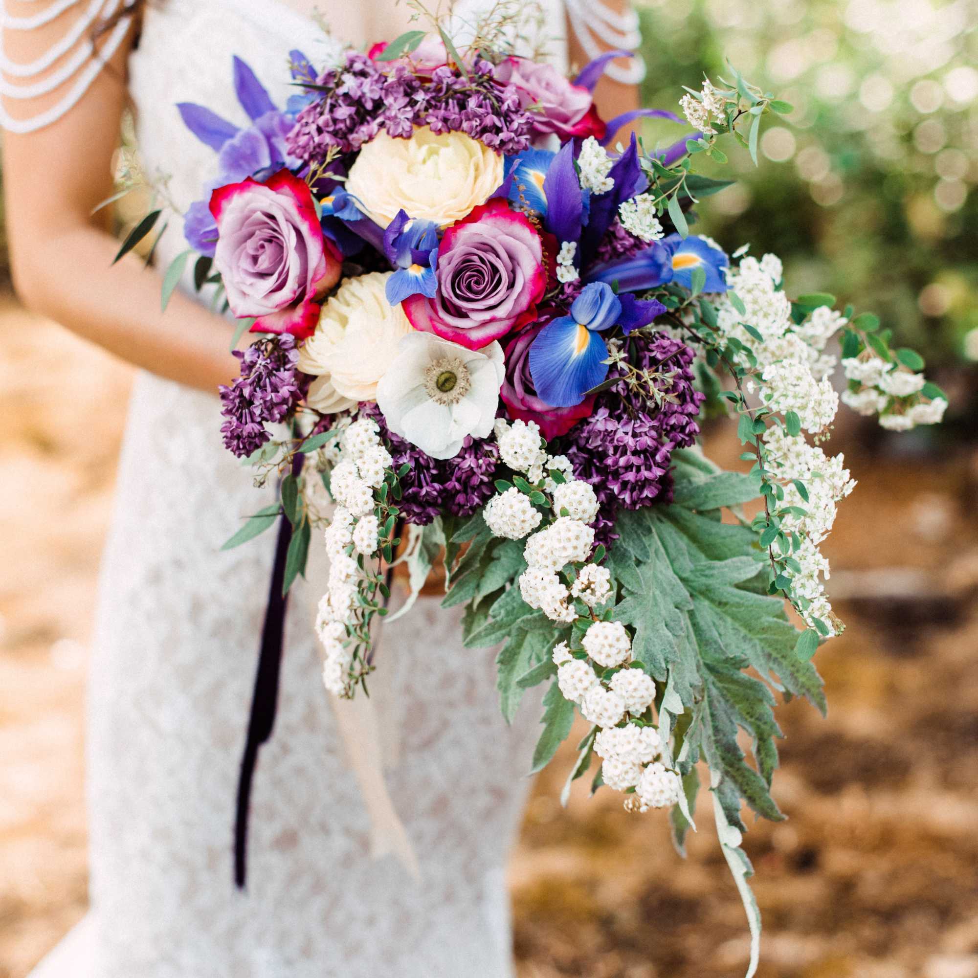 Bride holding a colorful bouquet of roses, anemones, and purple flowers