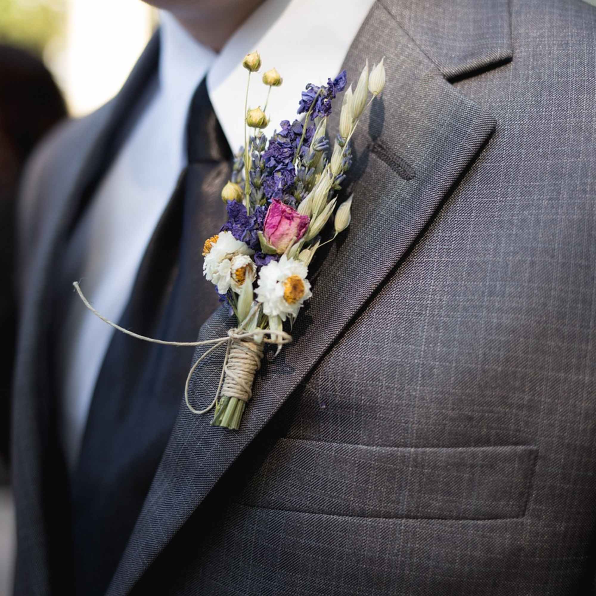 Small boutonniere with purple, white, and pink flowers on a suit lapel