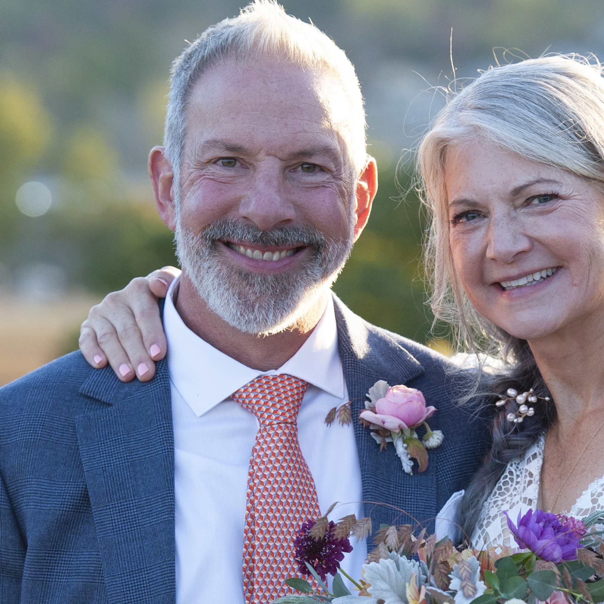 Smiling couple at a wedding with a pink boutonniere and bouquet