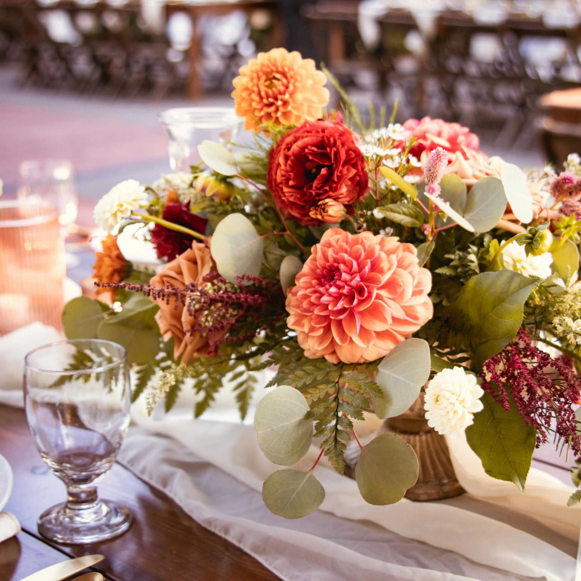 Low floral centerpiece with peach, red, and white blooms in a glass vase