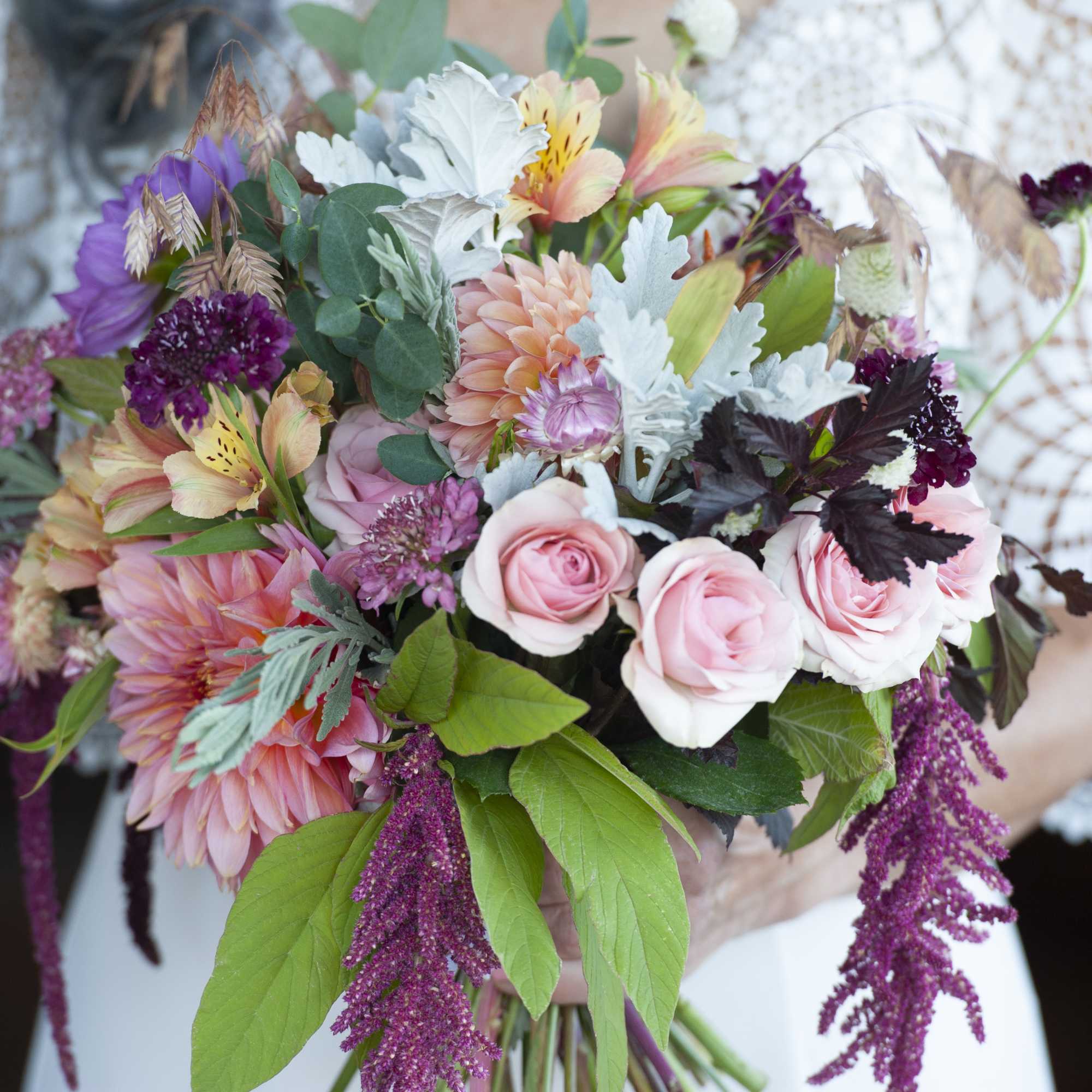 Handheld bouquet of pink roses, dahlias, and mixed blooms