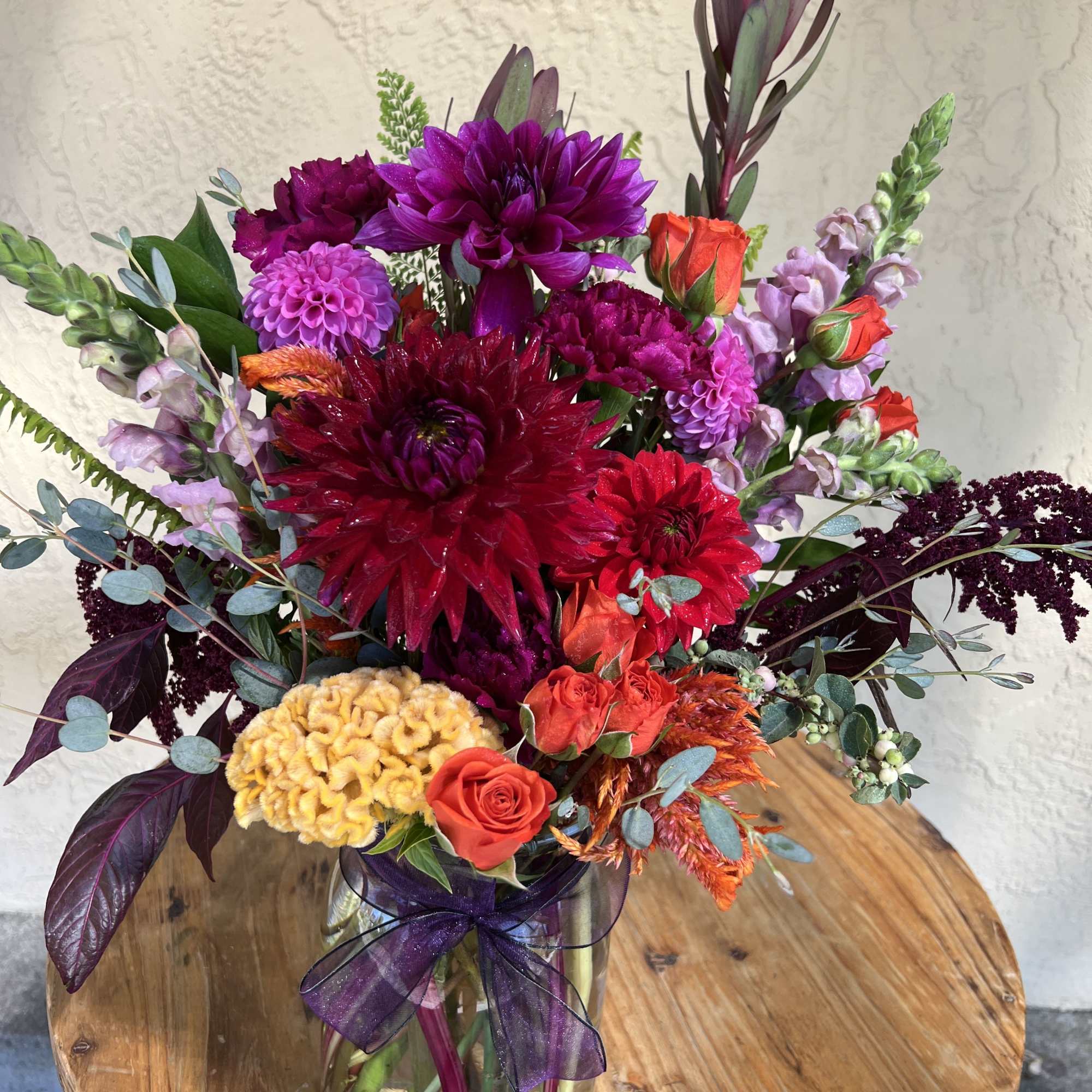 Colorful bouquet of dahlias and roses in a glass vase with a purple ribbon