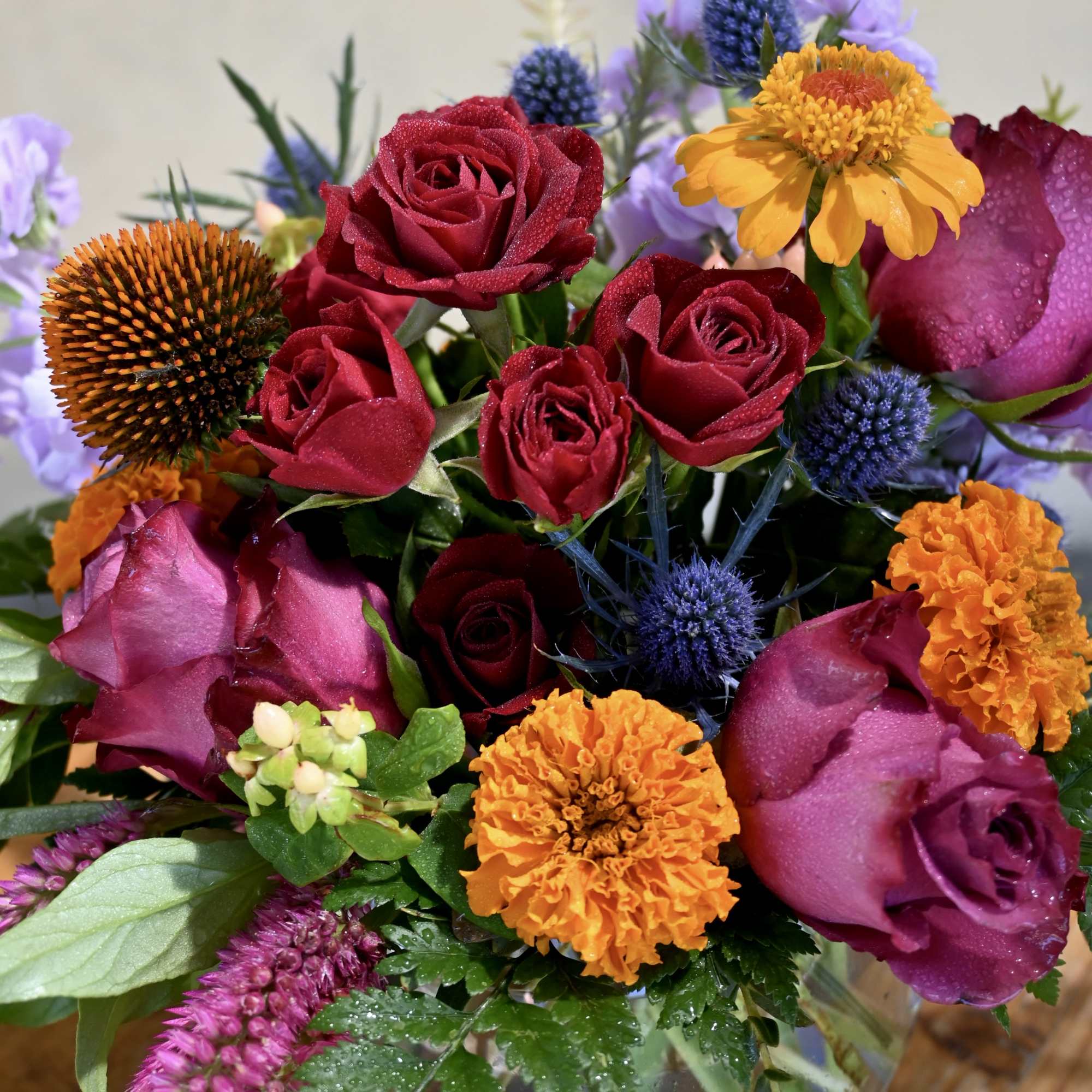 Mixed bouquet of red roses, orange marigolds, and purple flowers in a glass vase