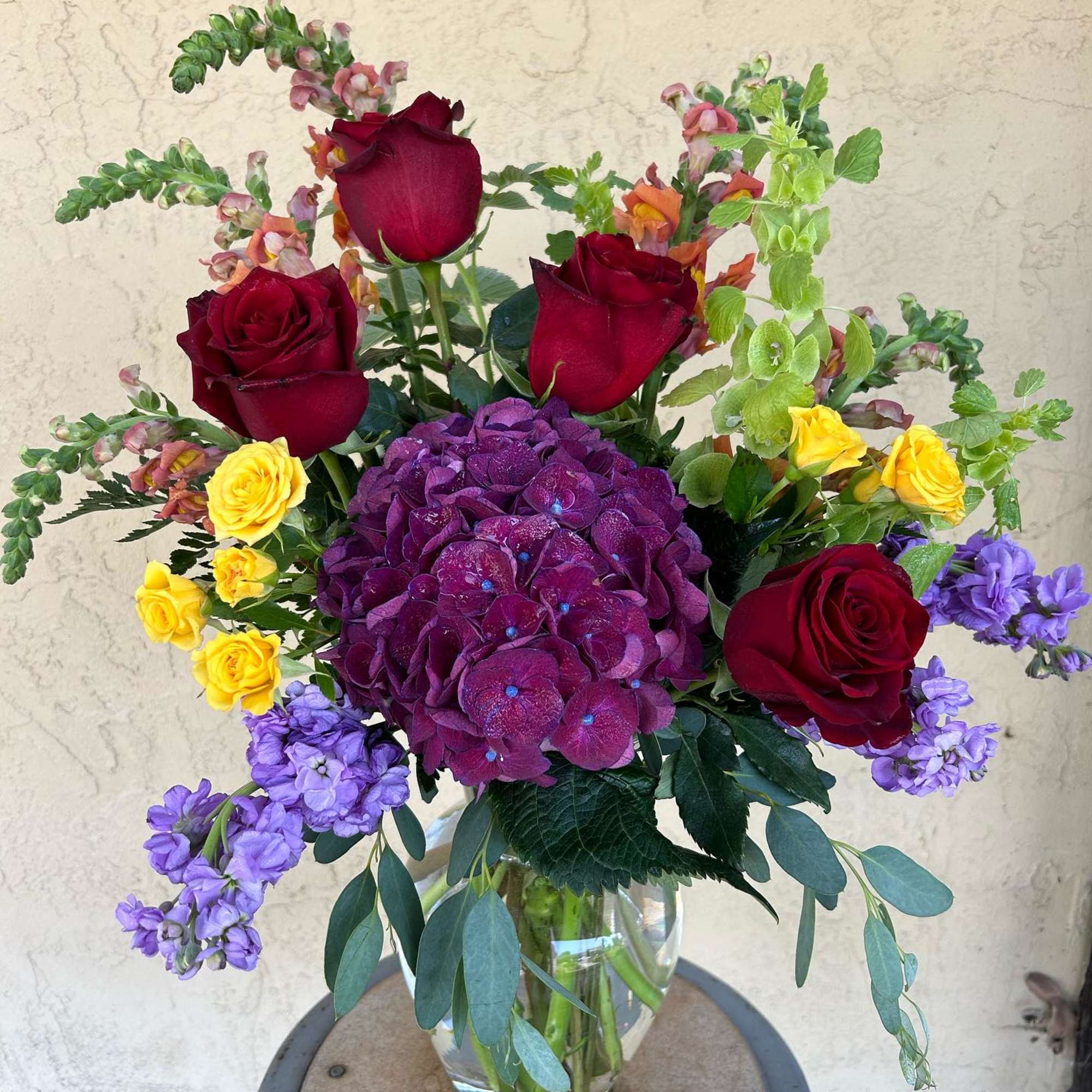 Bouquet of red roses, purple hydrangea, and yellow spray roses in a glass vase