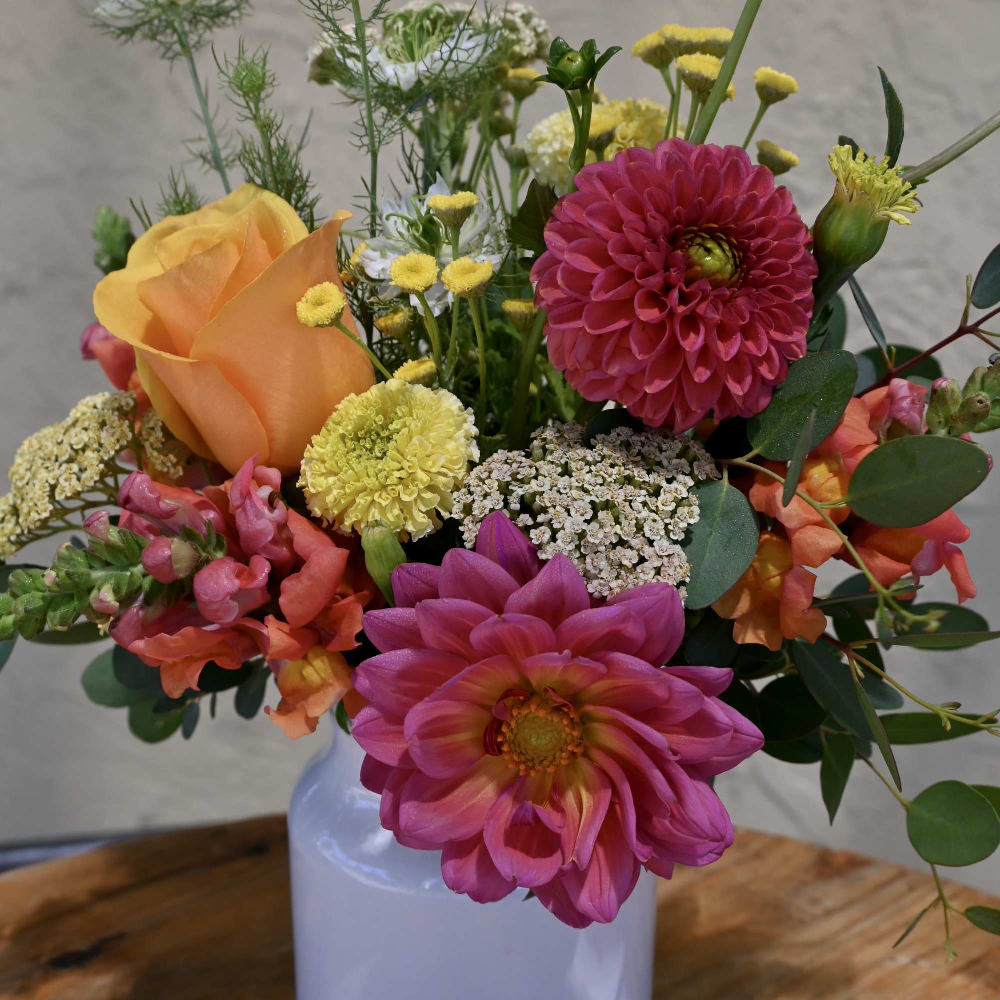 Mixed bouquet of pink, orange, and yellow flowers in a white vase