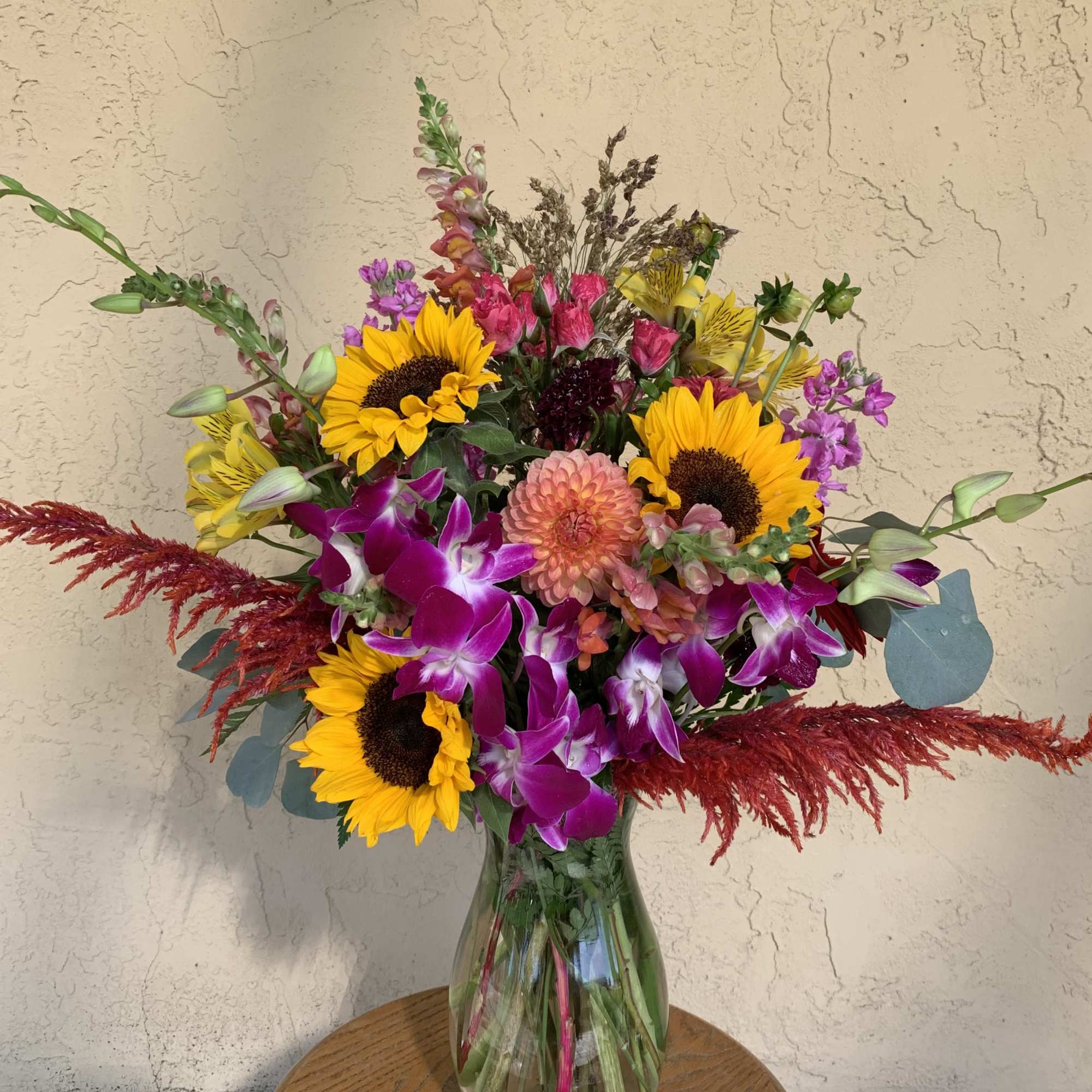 Mixed bouquet with sunflowers, orchids, and pink blooms in a glass vase