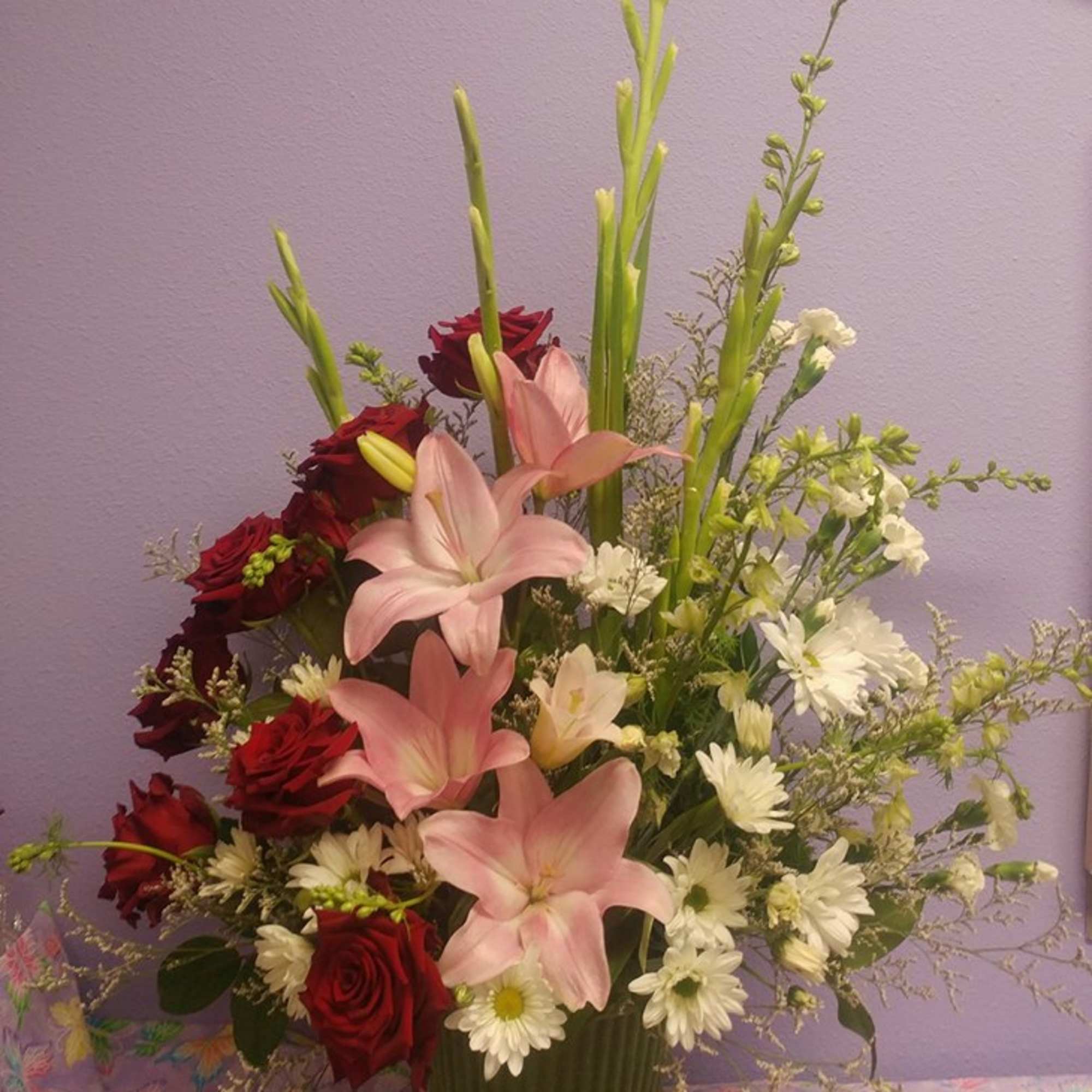 Pink lilies and red roses in a green vase with white daisies