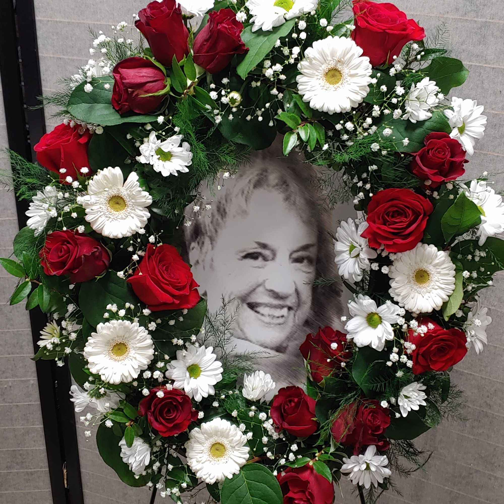 Heart-shaped wreath of red roses and white daisies around a portrait