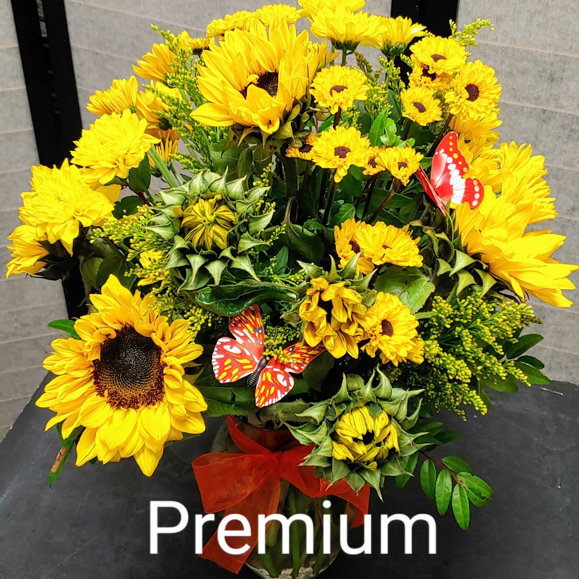 Yellow sunflower bouquet in a glass vase with red ribbon and butterfly picks
