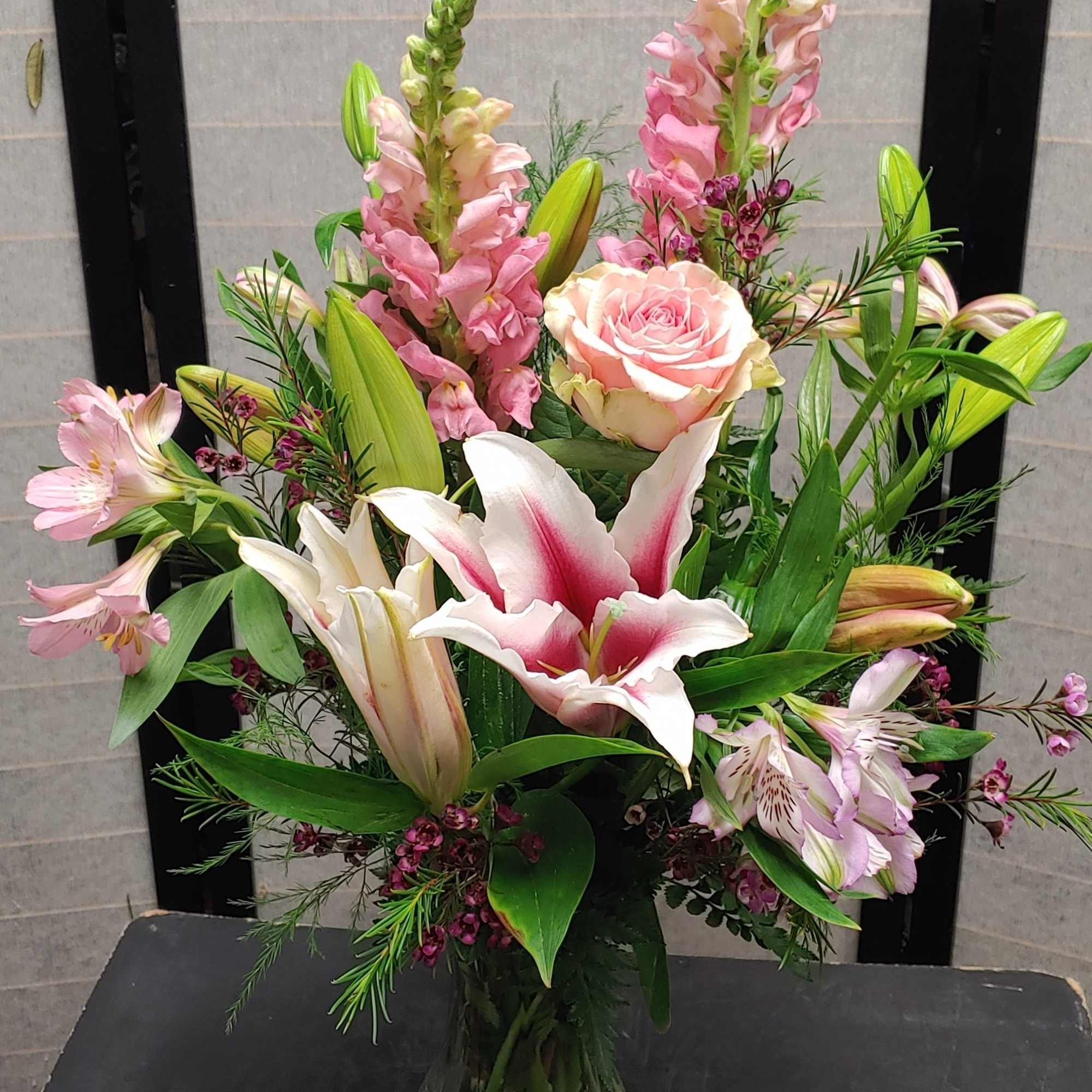 Pink and white floral arrangement with lilies, roses, and snapdragons in a glass vase