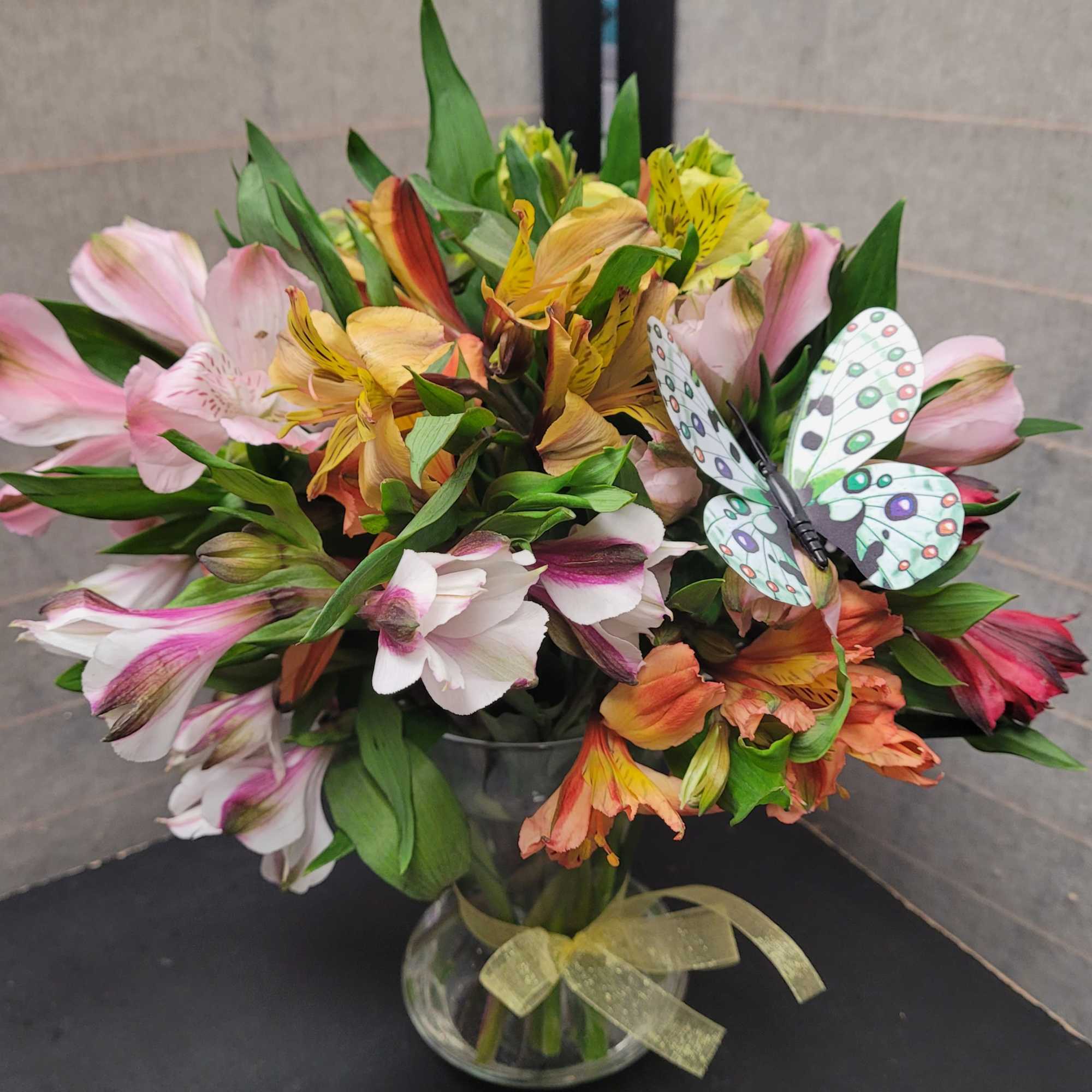 Mixed bouquet of alstroemeria in a glass vase with a butterfly decoration