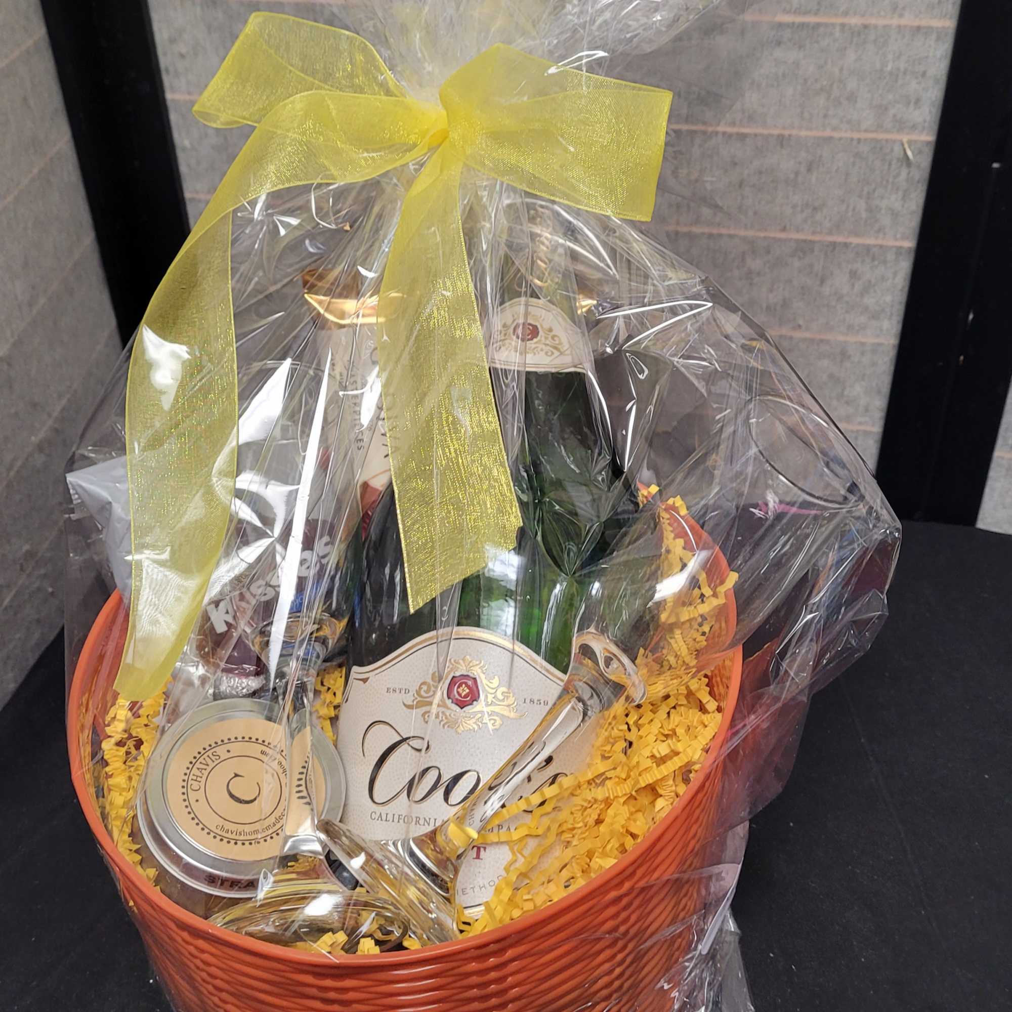 Gift basket with wine, a candle, and a glass under clear wrap with a yellow bow